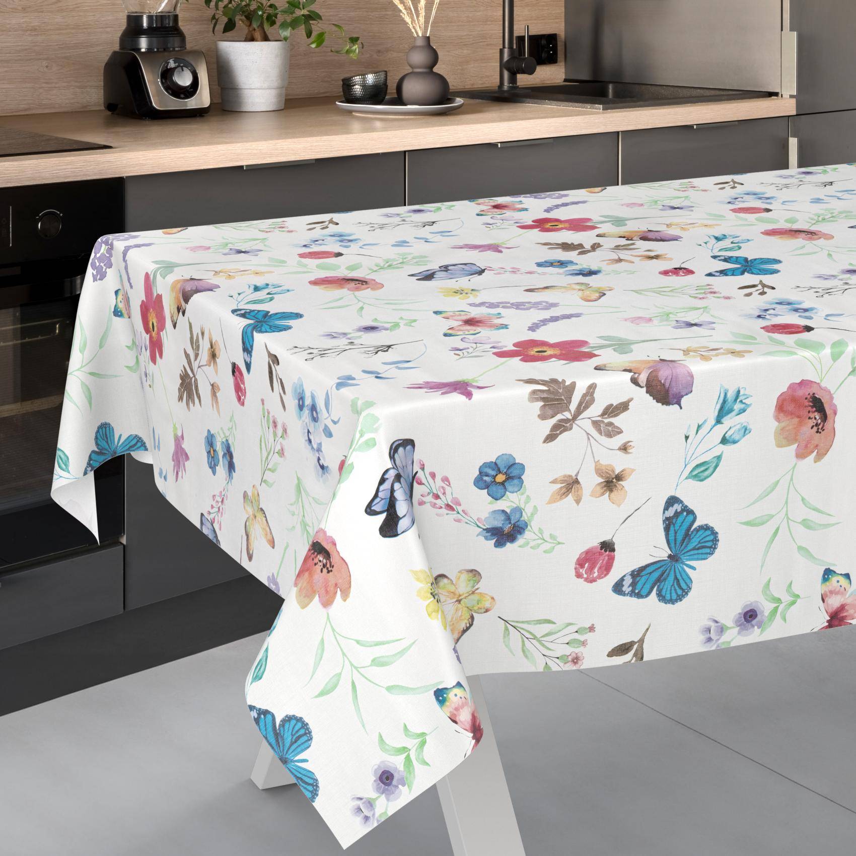 Weiße Tischdecke mit buntem Schmetterlings- und Blumenmuster, die über einen Tisch in einer modernen Küche drapiert ist.