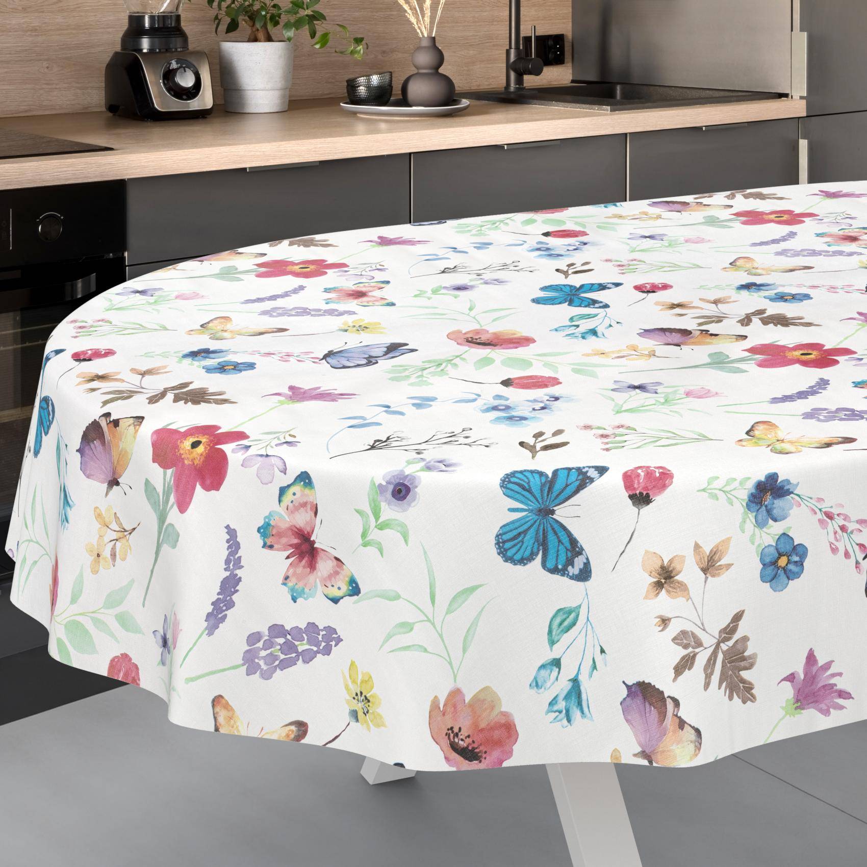 Runder Tisch mit einer weißen Tischdecke mit Blumen- und Schmetteringsmotiven in einer modernen Küche.