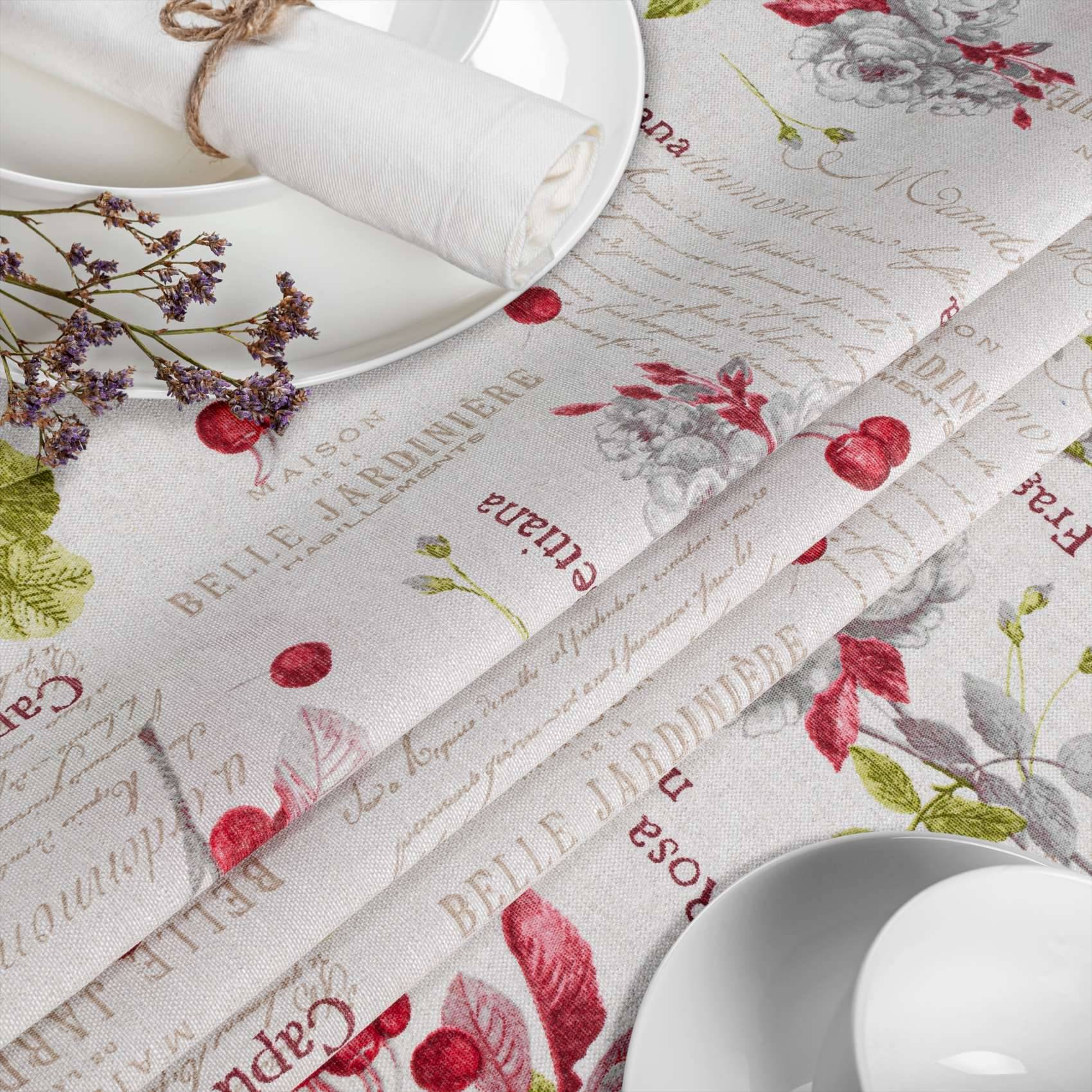 Tisch mit floralen Leinenservietten und Platzset, weißen Tellern und getrockneten Kräutern auf einer hell gemusterten Tischdecke eingedeckt.