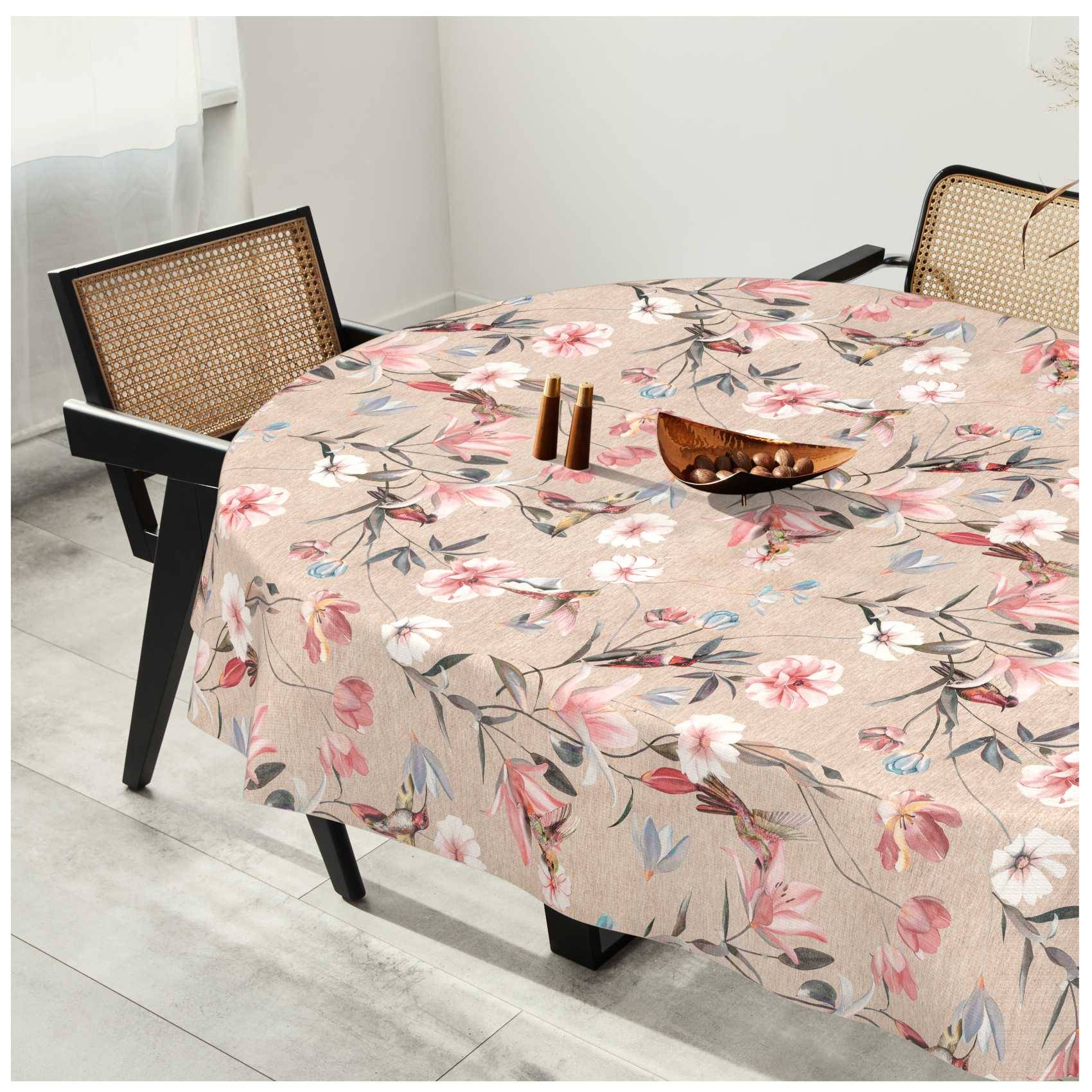 Ein runder Esstisch mit einer Blumentischdecke in einem hellen Raum, umgeben von Stühlen mit Flechtwerk-Rückenlehne und einfacher Tischdekoration.