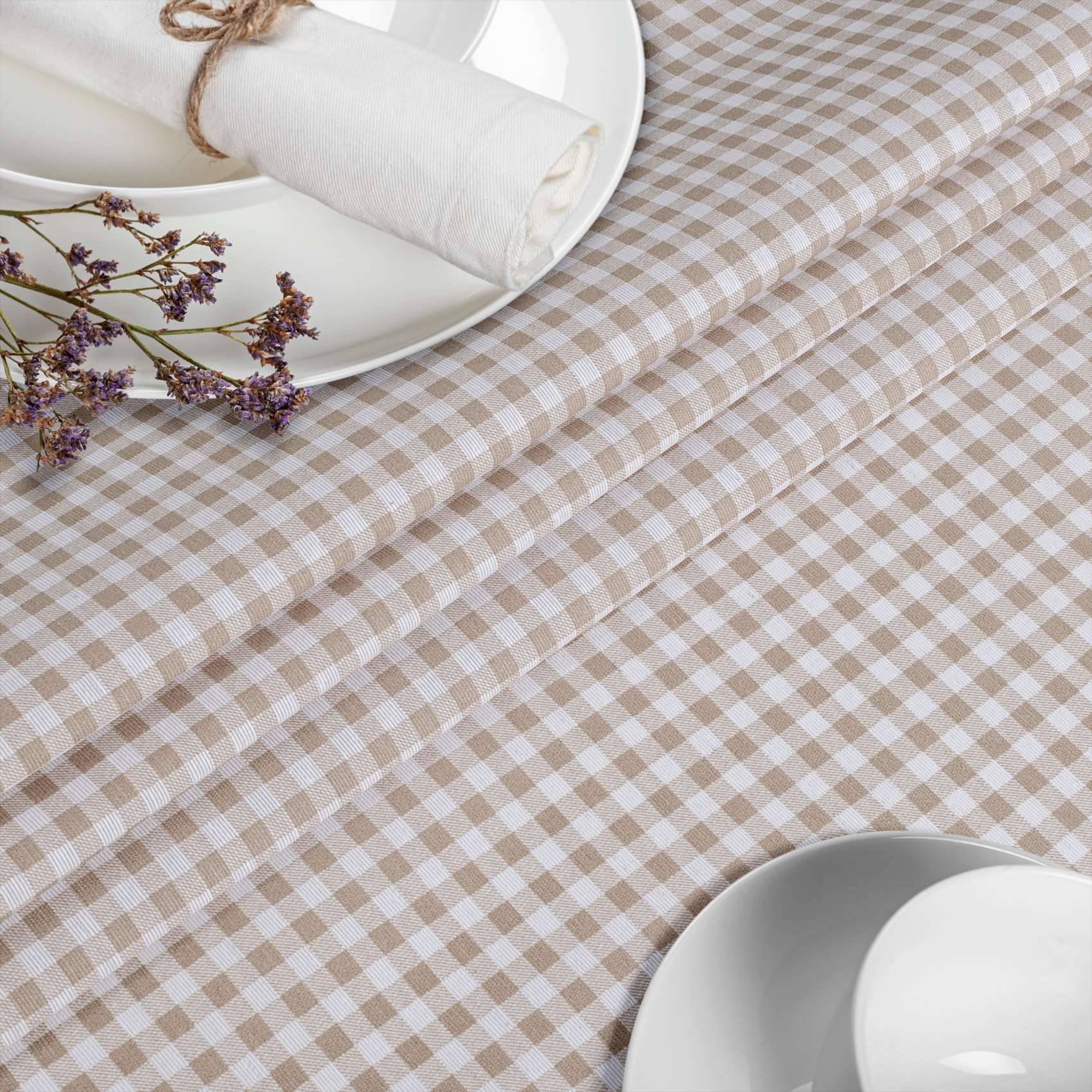 Beige Gingham-Tischdecke mit weißen Tellern, gerollten Servietten und einem kleinen Strauß getrockneter Blumen auf einem gedeckten Esstisch.