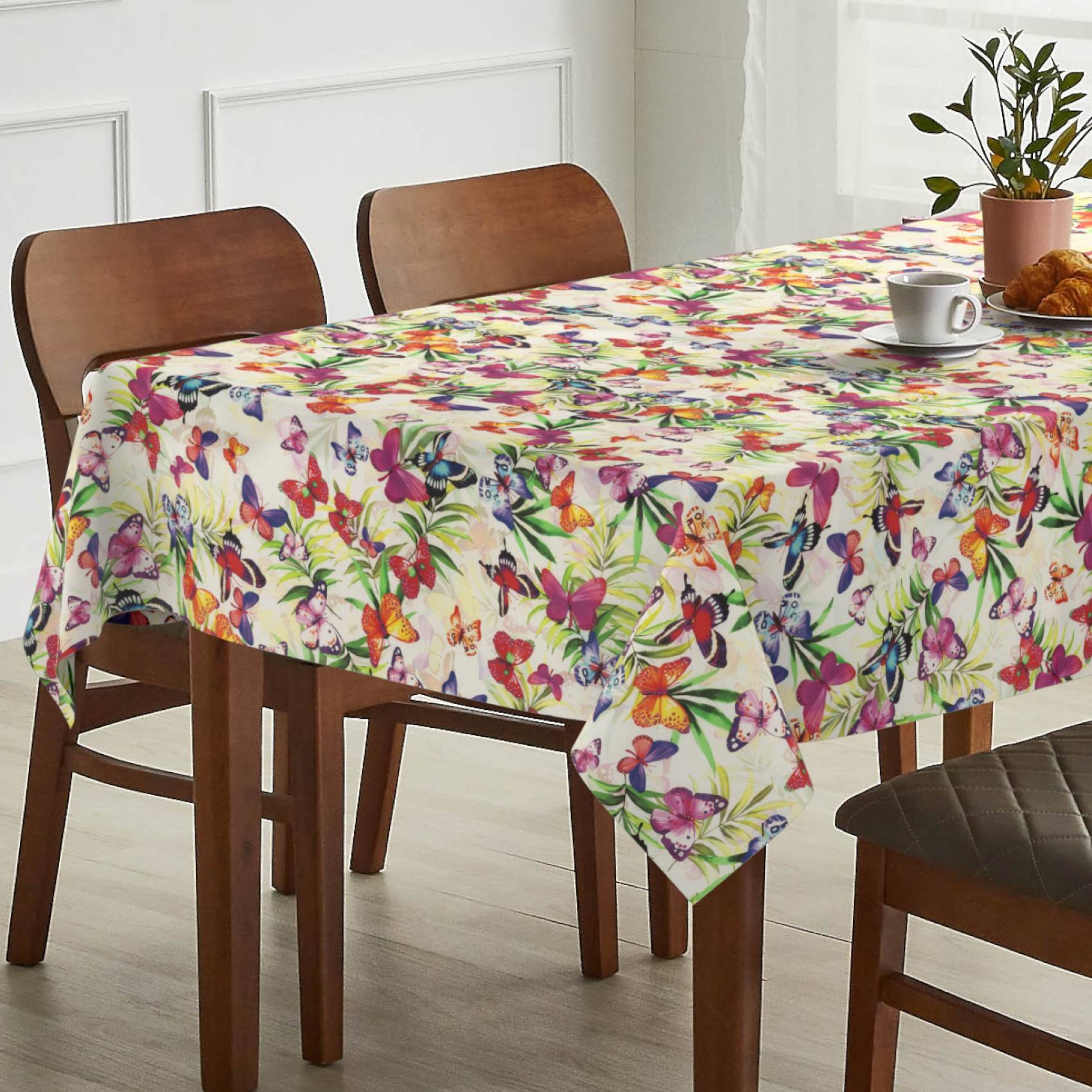 Esstisch mit einer bunten Schmetterlingsdrucktischdecke in einem hellen Esszimmer, mit Stühlen, einer Tasse und einer Pflanze auf dem Tisch.