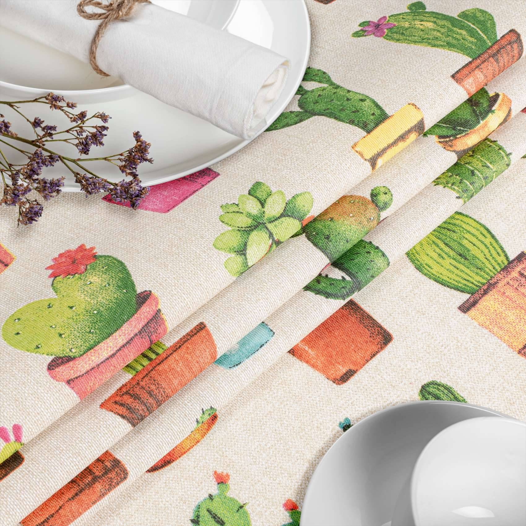Farbenfrohe Tischdecke mit Kaktusmuster auf einem Esstisch, mit weißen Tellern, aufgerollten Servietten und Lavendelzweigen, die zu einer Mahlzeit arrangiert sind.