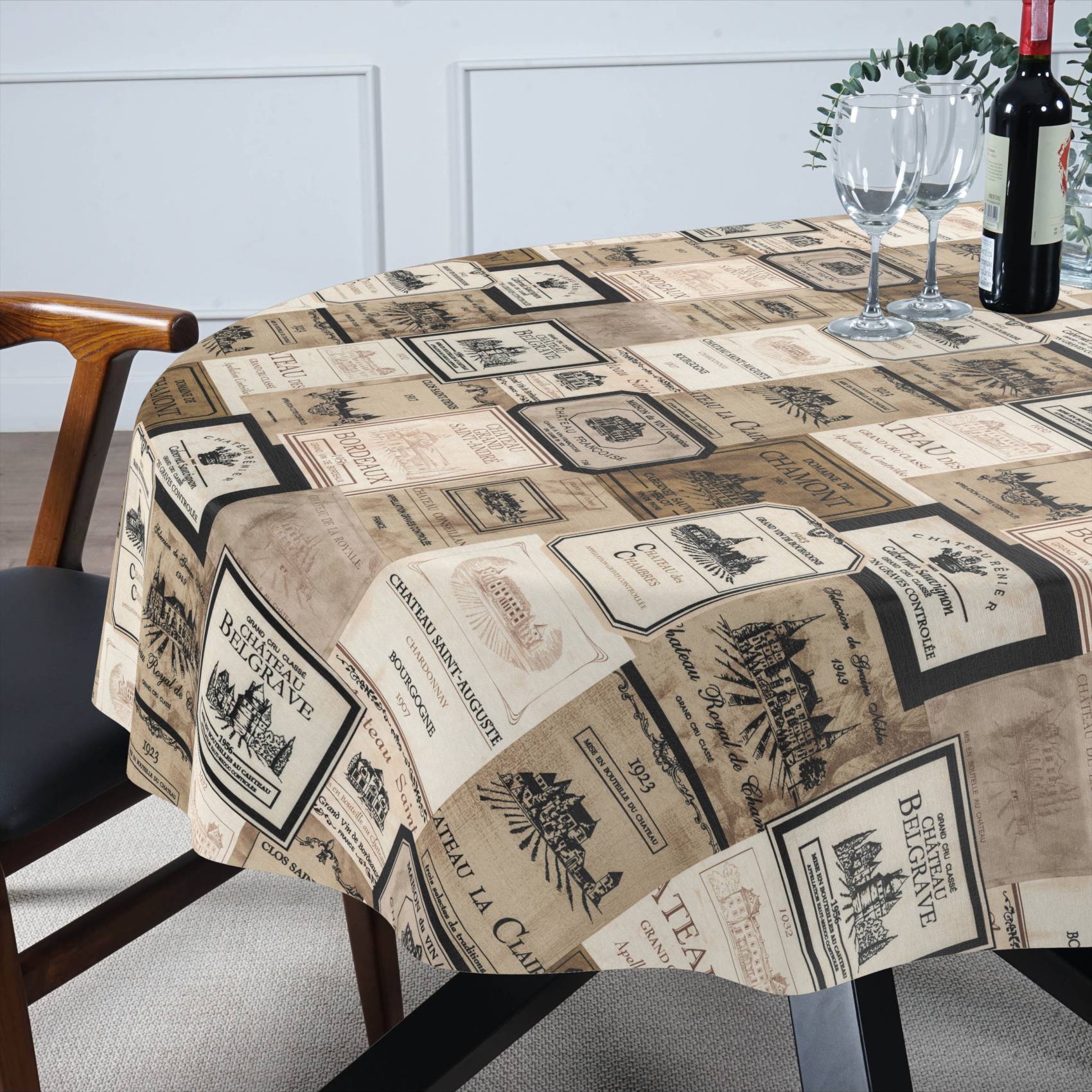 Ein Esstisch, bedeckt mit einer Tischdecke mit Vintage-Weinetikett-Muster, gedeckt mit zwei Weingläsern und einer Flasche Rotwein.