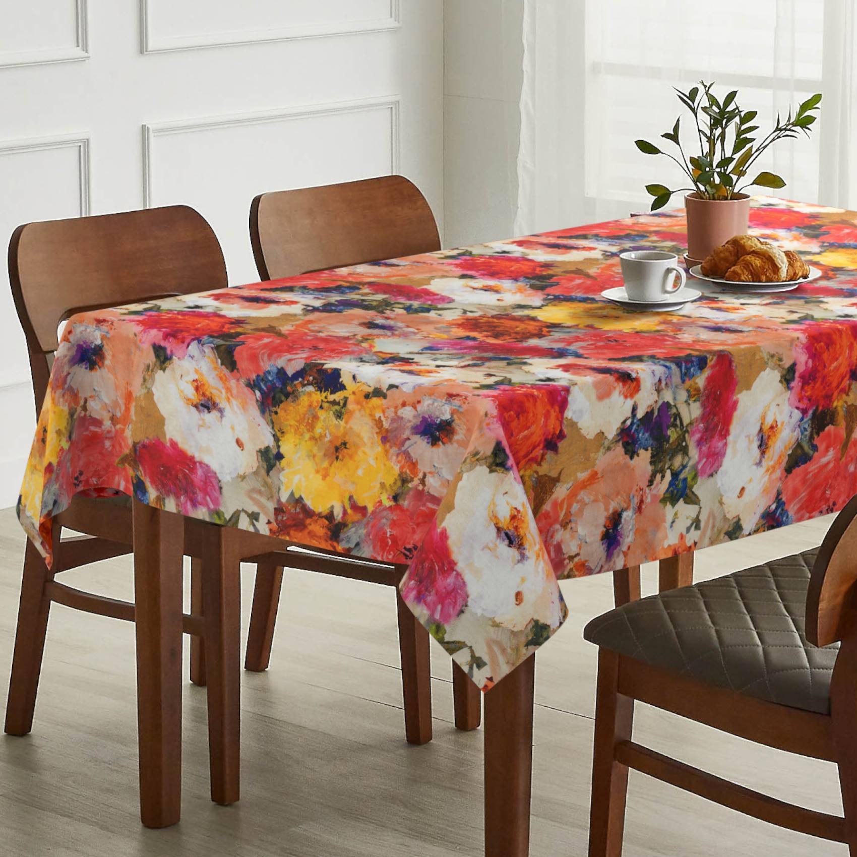 Esstisch mit farbenfrohem abstraktem Blumen-Tischdecke, eingedeckt mit einer Tasse und einem Croissant auf einem hellen, modernen Esstisch.