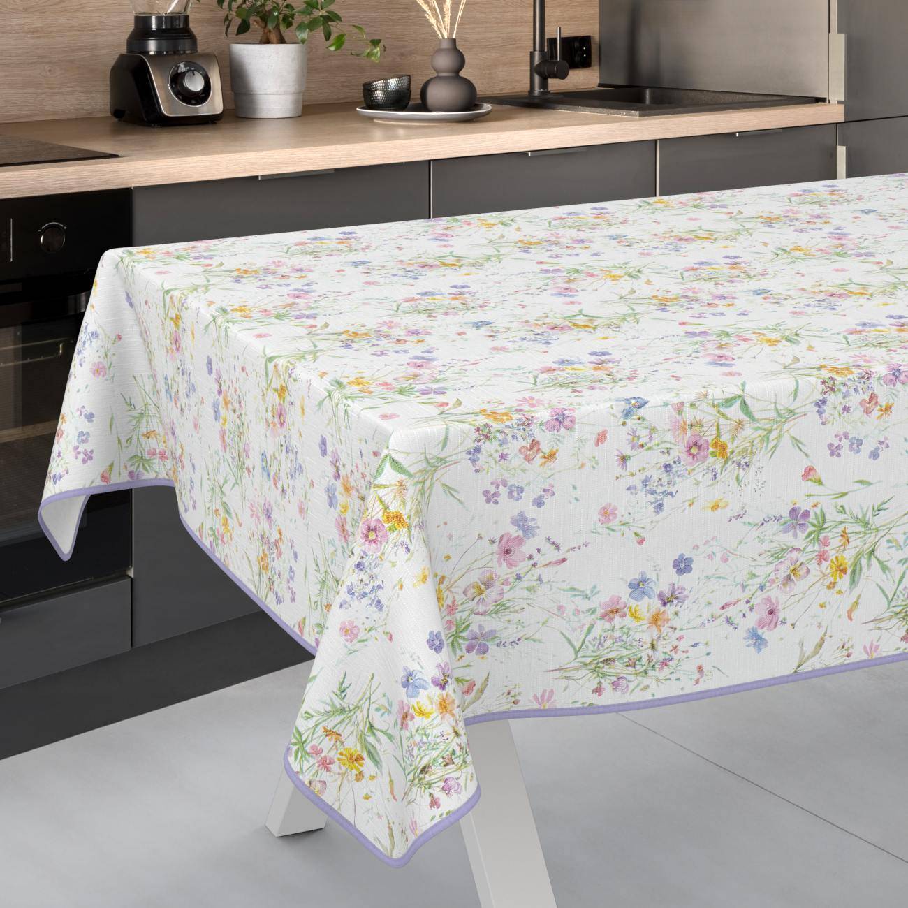 Rechteckiger Esstisch mit einer weißen Tischdecke mit Blumenmuster und Lavendelkante in einer modernen Küche.