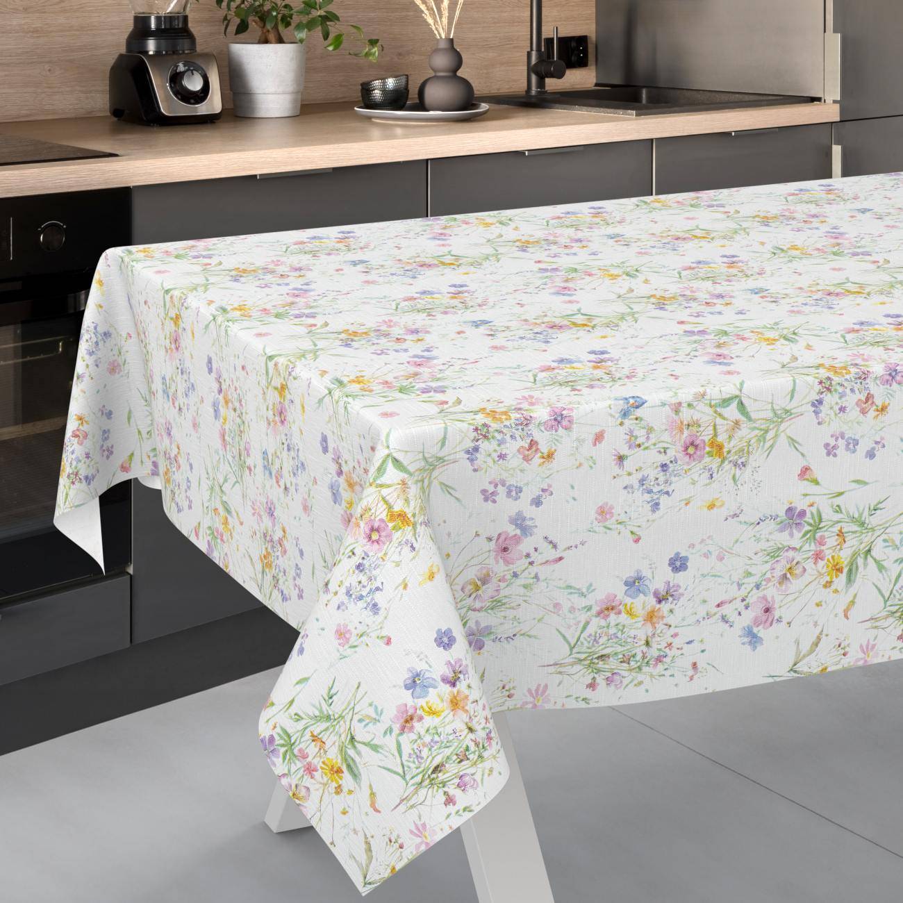 Ein Küchentisch, der mit einer weißen Tischdecke mit Blumenmuster bedeckt ist, die über die Kanten herabfällt.