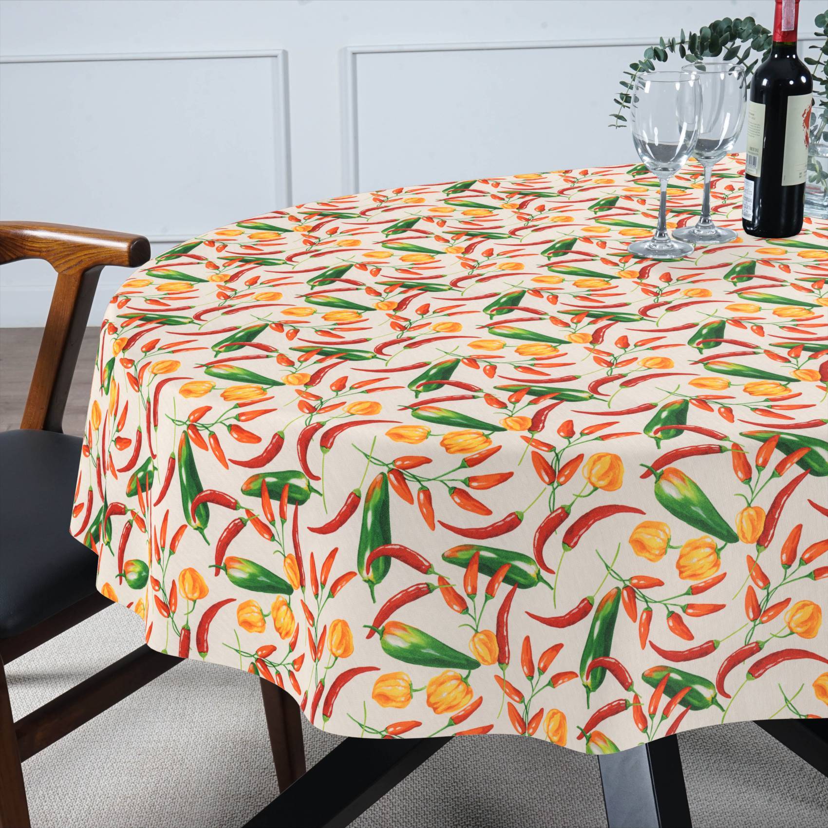 Ein runder Esstisch, bedeckt mit einer bunten Tischdecke mit Chili-Pfeffer- und Blumenmuster, mit Weingläsern und einer Flasche, die zum Essen gedeckt ist.