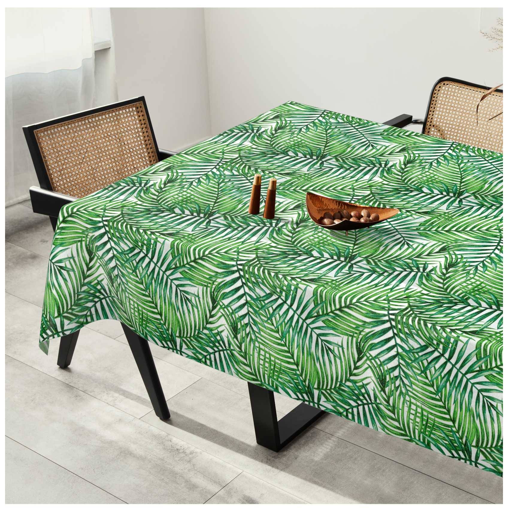 Esstisch mit einer grünen Tischdecke mit tropischem Blattmuster, zwei Stühle mit gewebtem Rückenlehnen und einfacher Mittelpunkt-Dekoration.