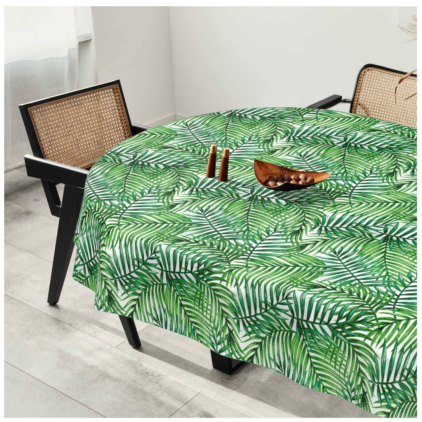 Runder Esstisch mit grüner Palmblatt-Tischdecke, zwei Stühle mit gewebtem Rückenlehnen und eine kleine Holzschale in einem hellen Raum.