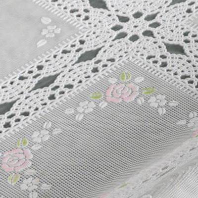 Nahaufnahme eines mit Spitze gesäumten Stoff-Kissens oder Polsters mit einem pastellrosa Blumenmuster auf grauem netzartigem Material.