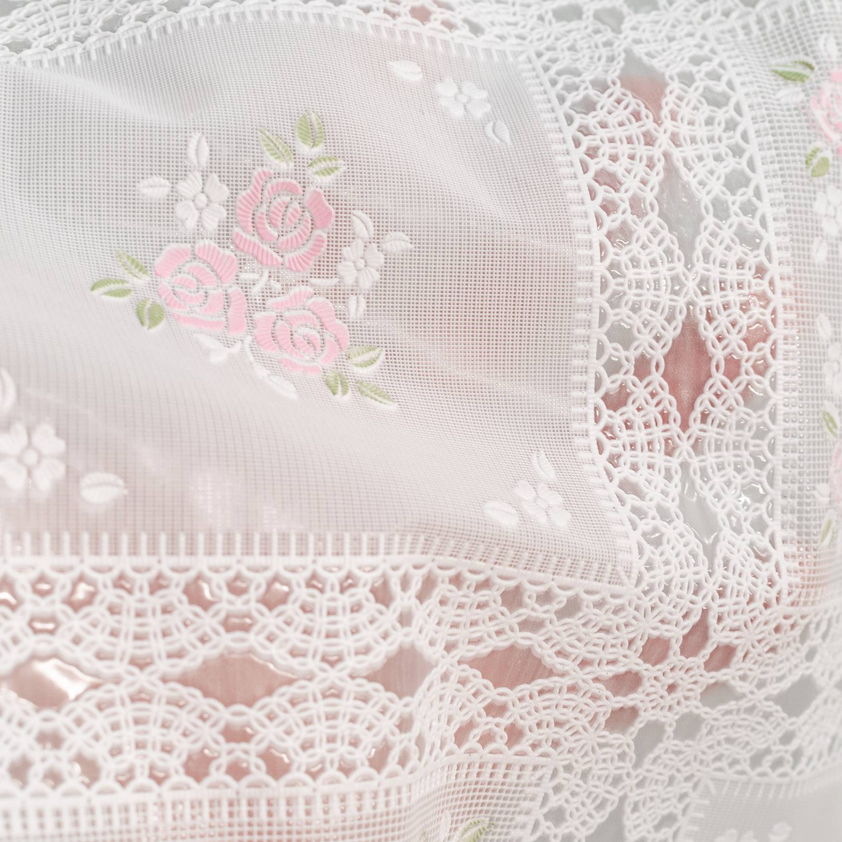 Nahaufnahme von weißem Spitzenstoff mit zarter rosa Rosenbestickung und Blumenbordüre.