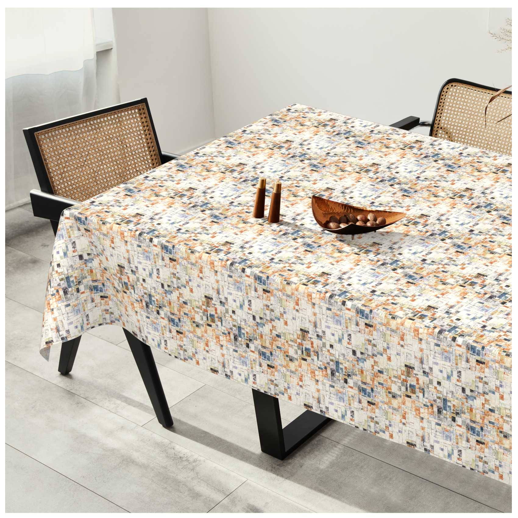 Esstisch mit einer mehrfarbig gemusterten Tischdecke bedeckt, mit zwei Holzstühlen und einer kleinen Schüssel als Tischdekoration in einem hellen Raum.