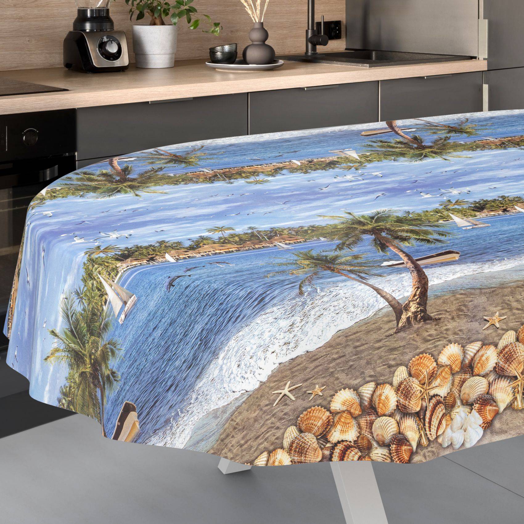 Ein Esstisch, der mit einer Tischdecke mit tropischem Strandmuster bedeckt ist, auf der Meereswellen, Palmen, Sand und Muscheln zu sehen sind.