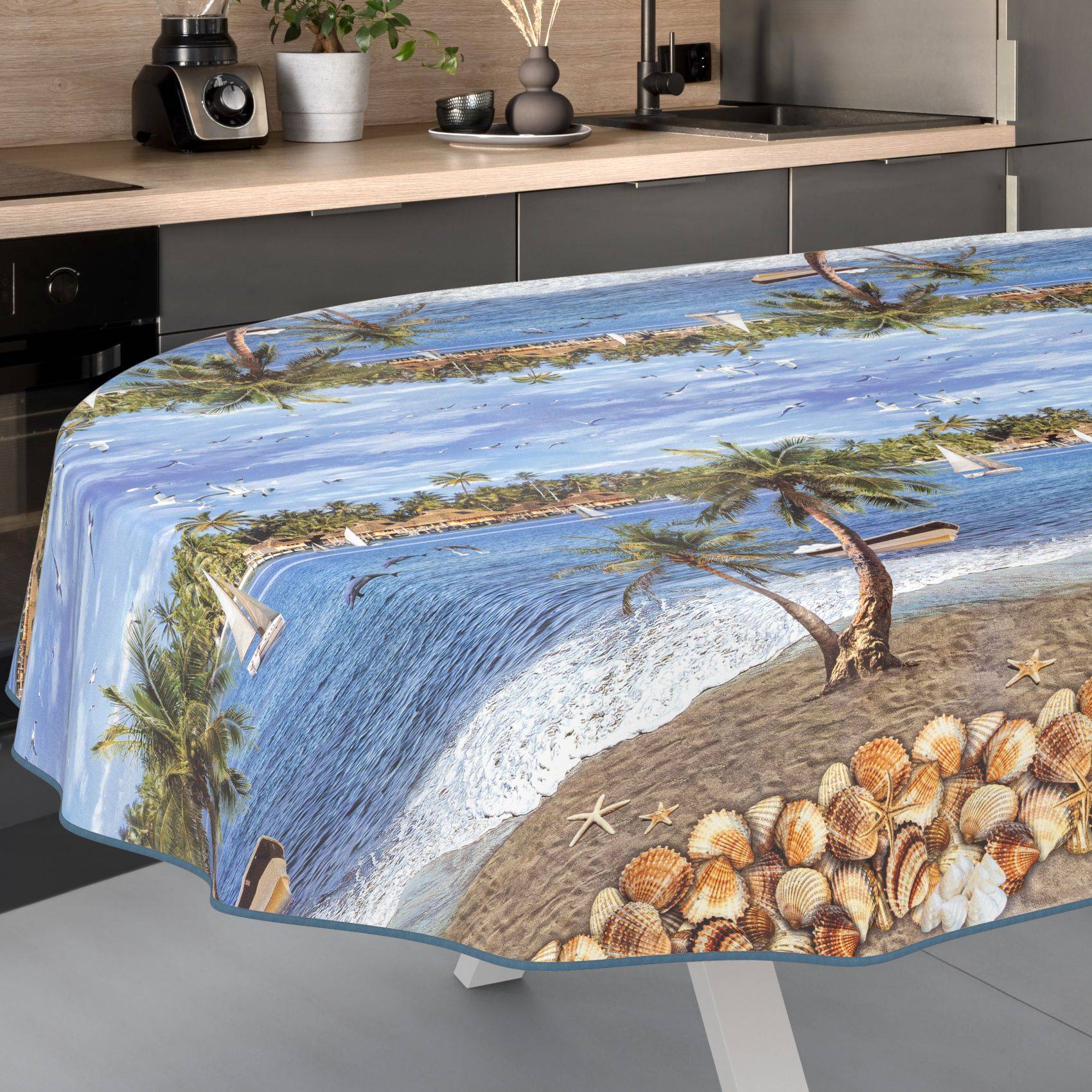 Ein Esstisch, der mit einer strandthematischen Tischdecke bedeckt ist, die Ozeanwellen, Palmen, Muscheln und eine Küstenszene zeigt.