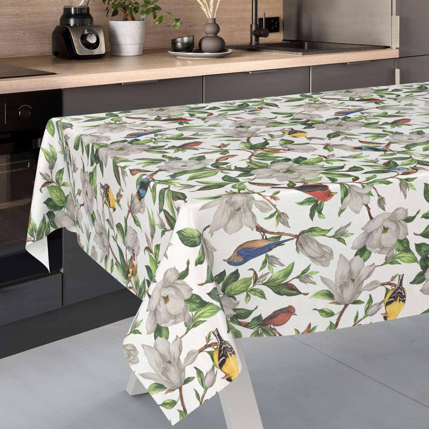 Tischdecke mit Vogel- und Blumenmuster, die über einen Esstisch in einer modernen Küche drapiert ist.