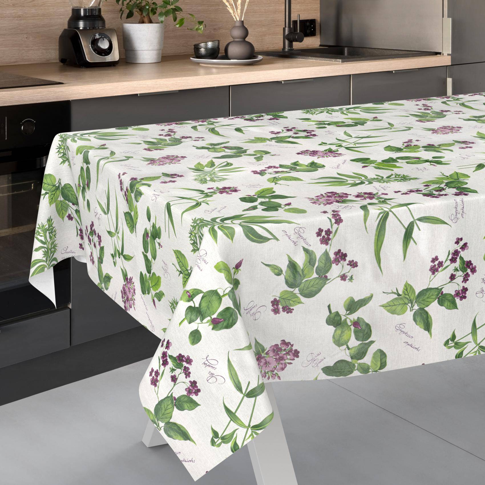 Küchentisch mit einer weißen Blumen-Tischdecke mit grünen Blättern und violetten Blüten.