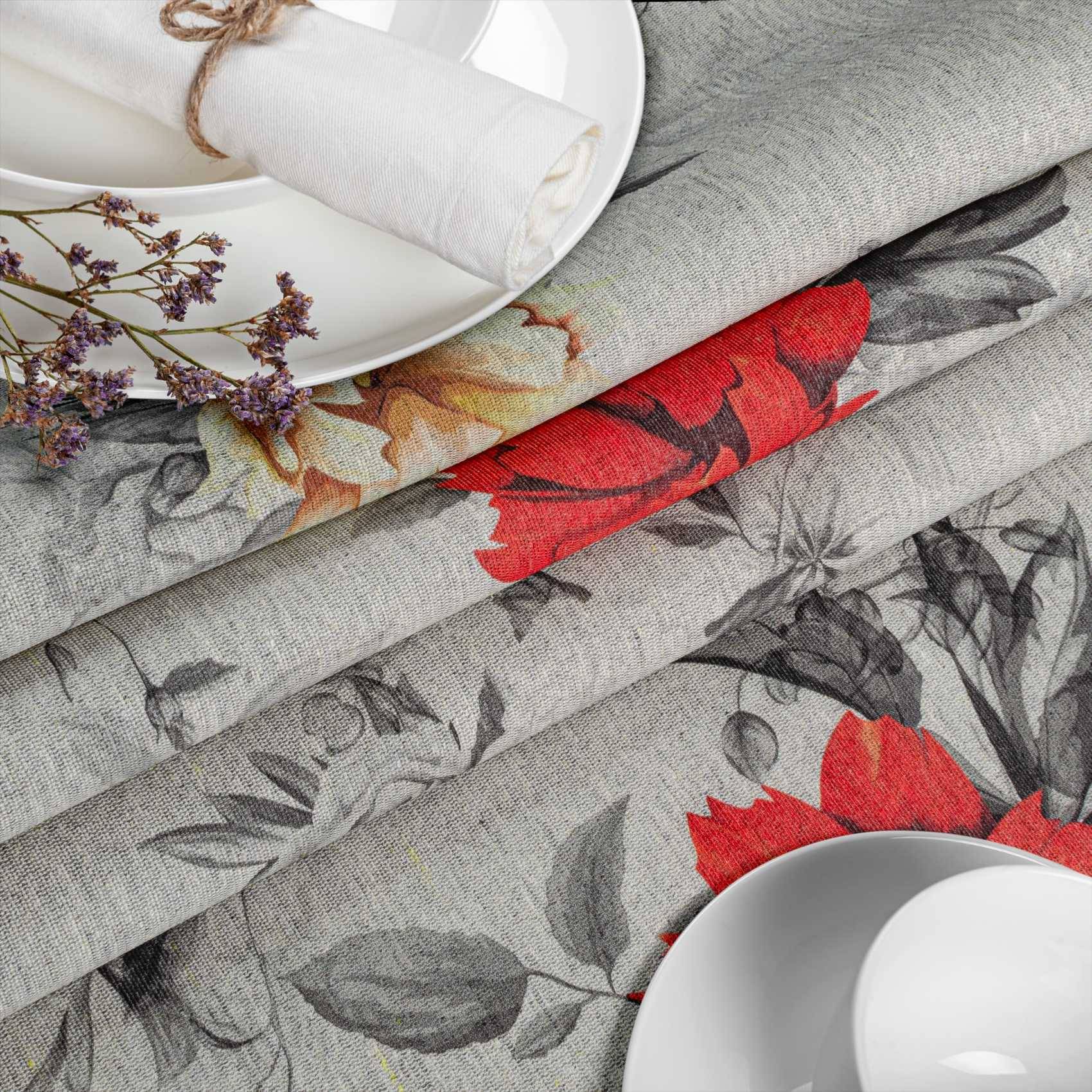 Gestapelte Stoffrollen mit Blumenmuster in Grau, Rot und Schwarz, mit weißen Tellern und Servietten, die oben angeordnet sind und eine Textil- oder Tafelgeschirr-Präsentation andeuten.