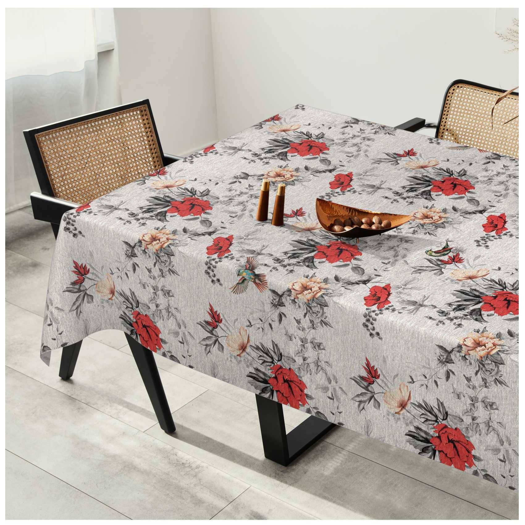 Esstisch mit einer grauen Tischdecke mit roten und pfirsichfarbenen Blumenmuster, in einem hellen Raum mit geflochtenen Stühlen.