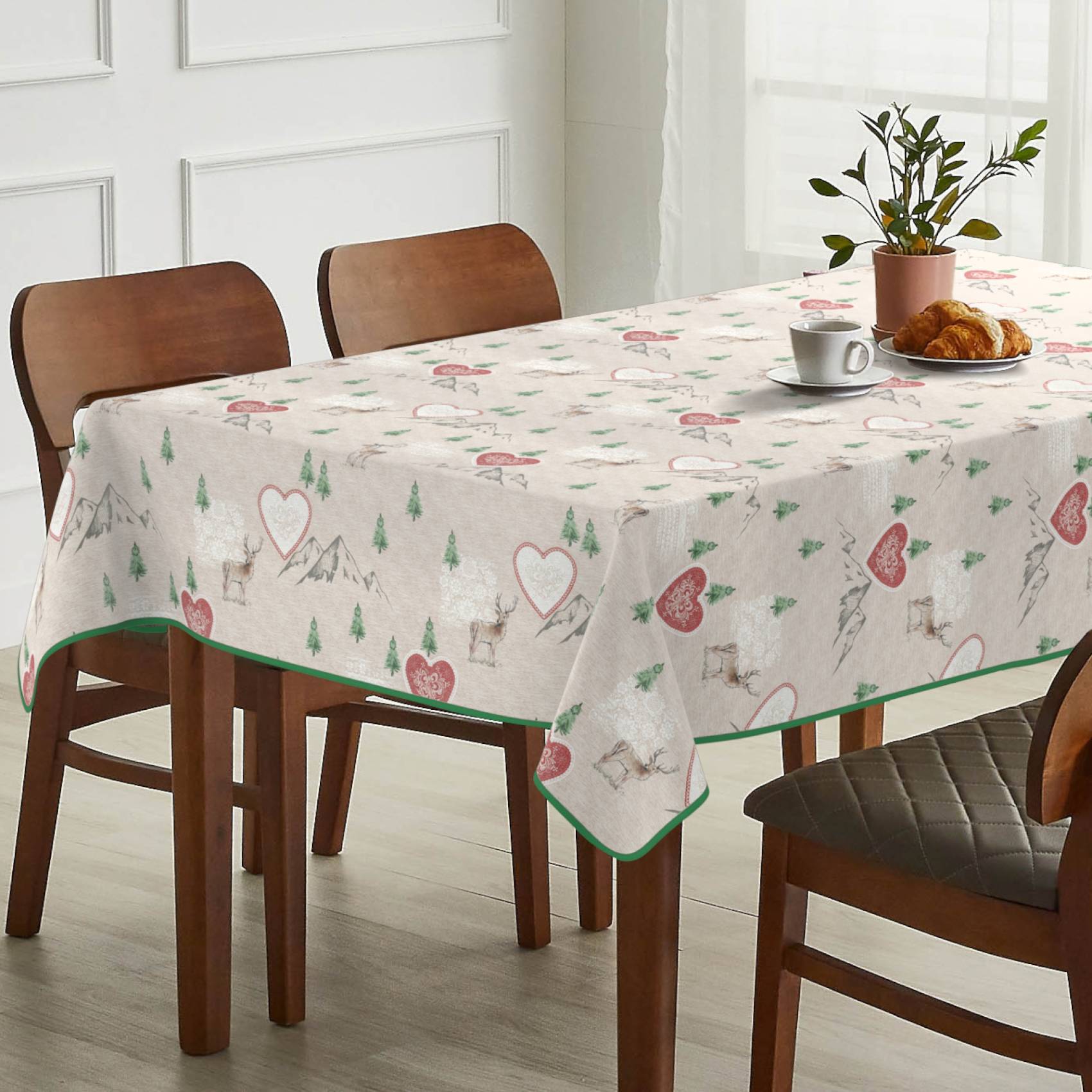 Esstisch mit weiß gemusterter Herz-und-Baum-Tischdecke, eingedeckt mit einer Kaffeetasse, einem Croissant und einer Topfpflanze in einem hellen Raum