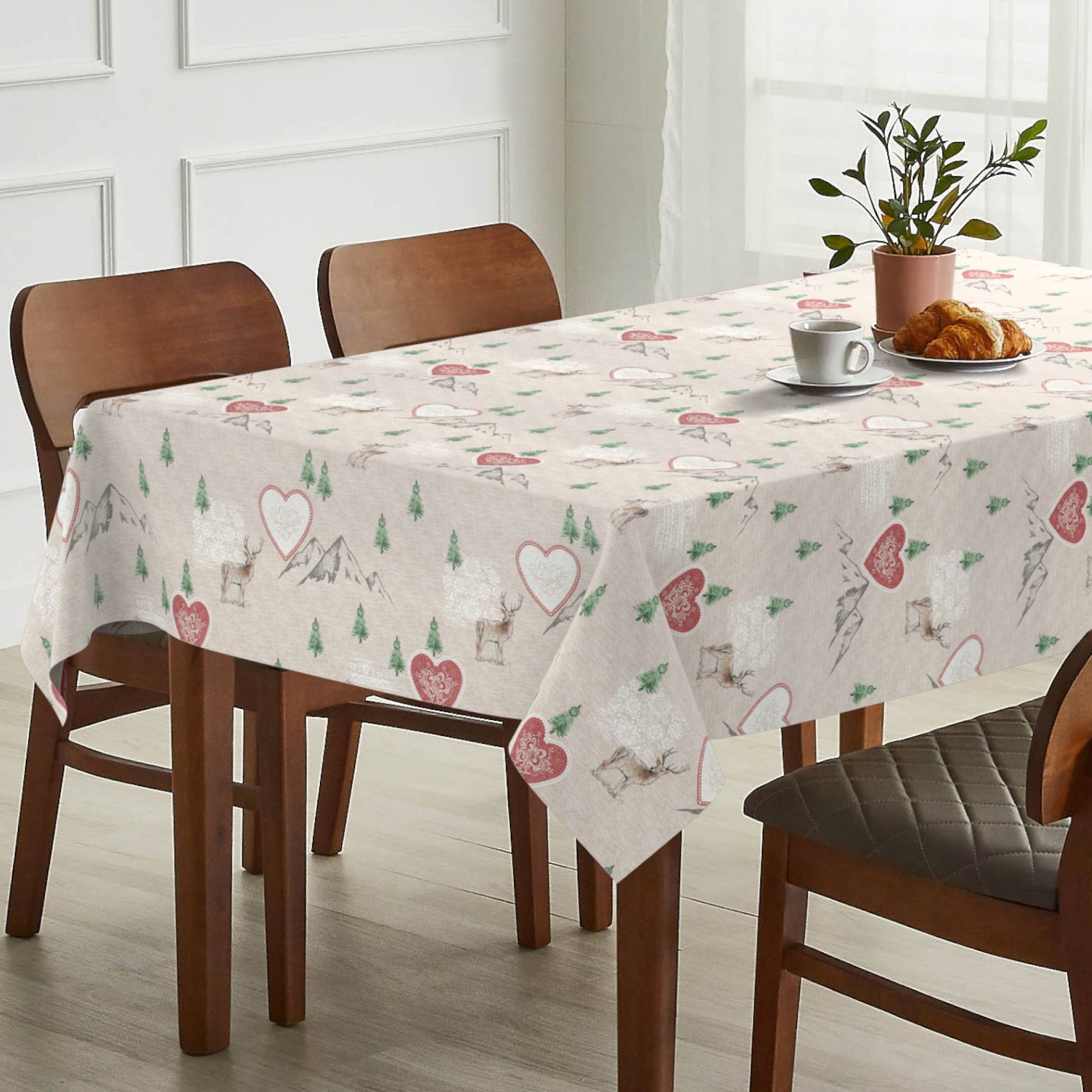 Esstisch mit einer Tischdecke mit Herzenmuster, eingedeckt mit einer Tasse, Croissants und einer Topfpflanze in einem hellen Raum mit Holzstühlen.