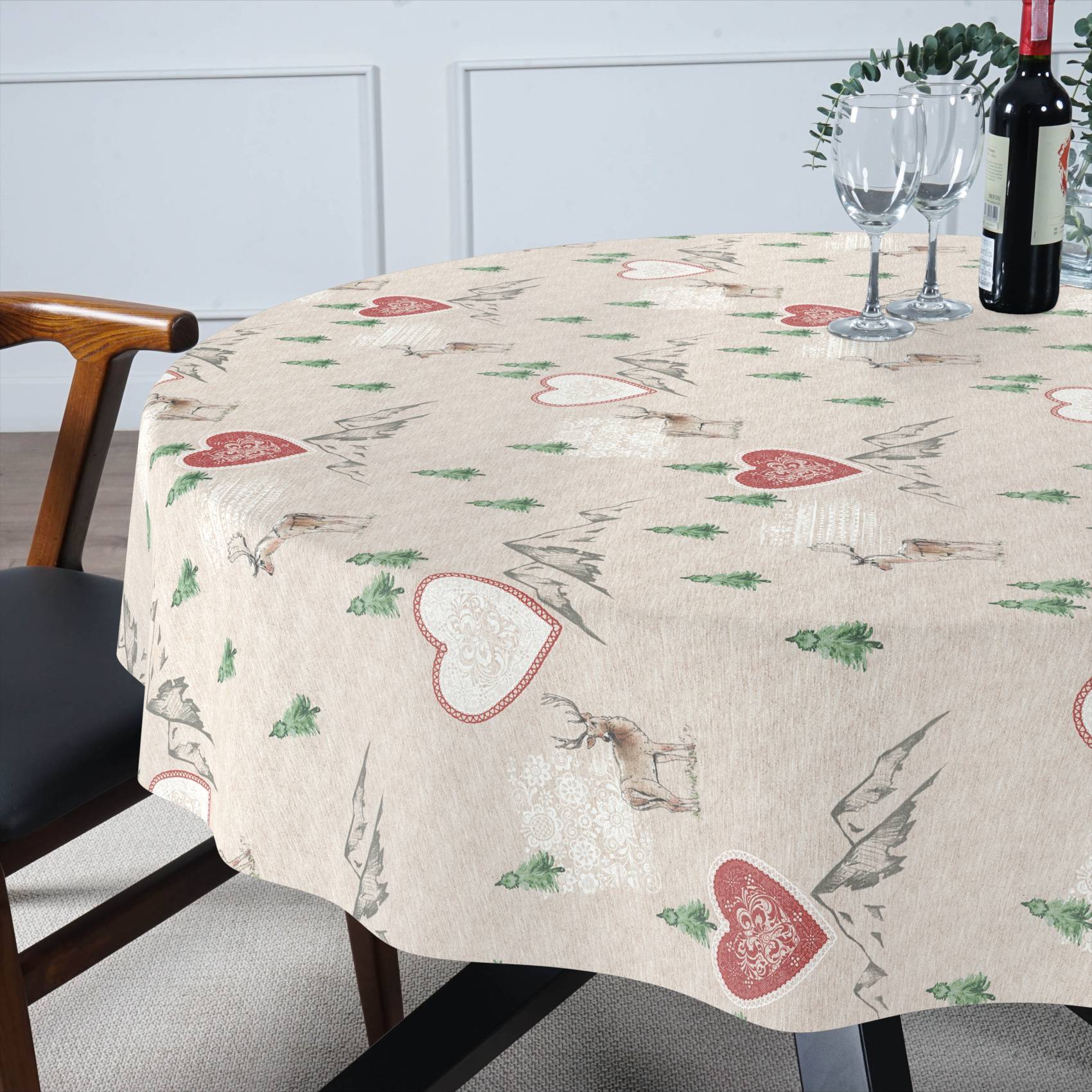 Runder Tisch mit beiger Tischdecke mit Herzenmuster, eingedeckt mit Weingläsern und einer Flasche neben einem Holzstuhl in einem hellen Speisezimmer.