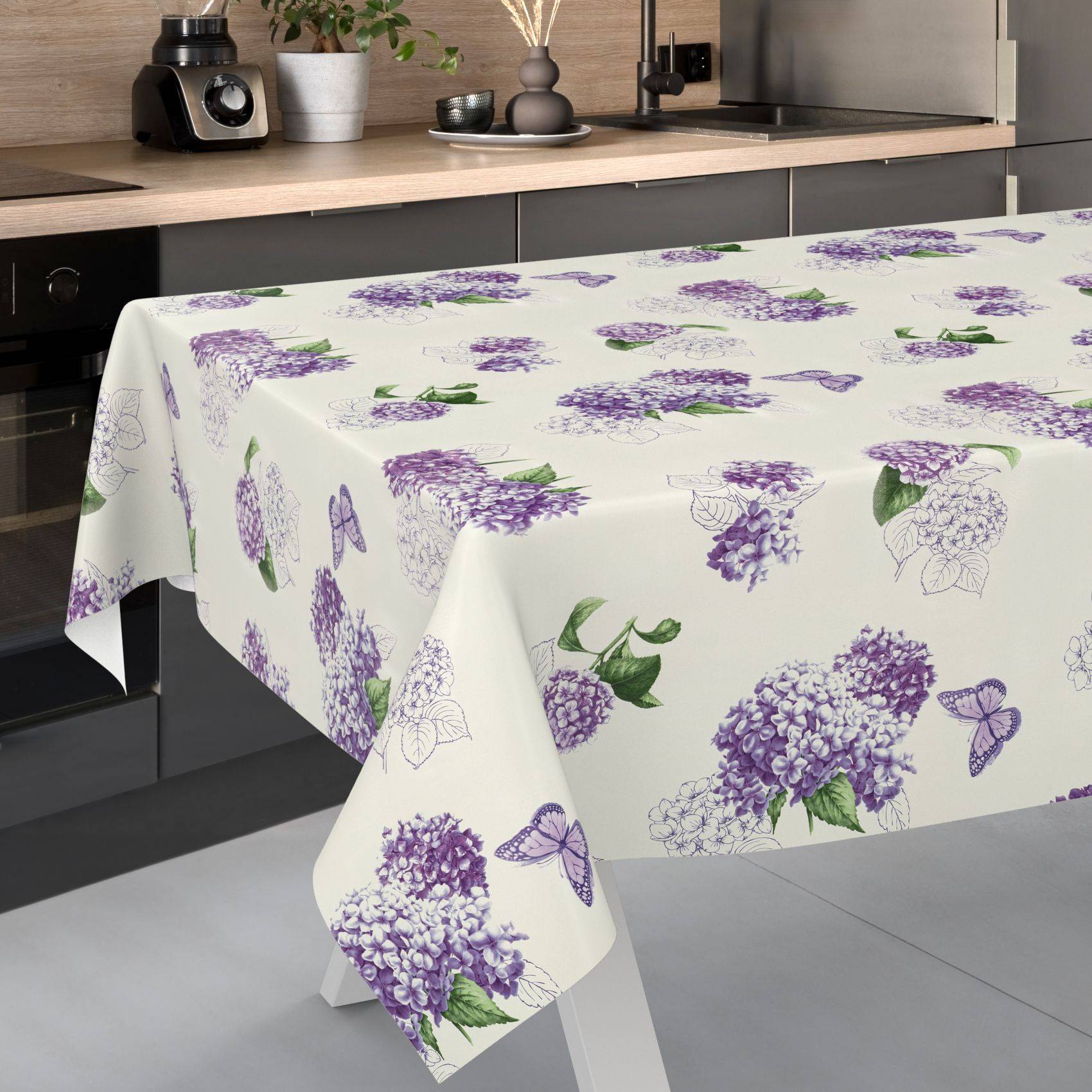 Tischdecke mit violettem Flieder- und Schmetterlingsmuster, das über einem Küchentisch in einer modernen Küche drapiert ist.