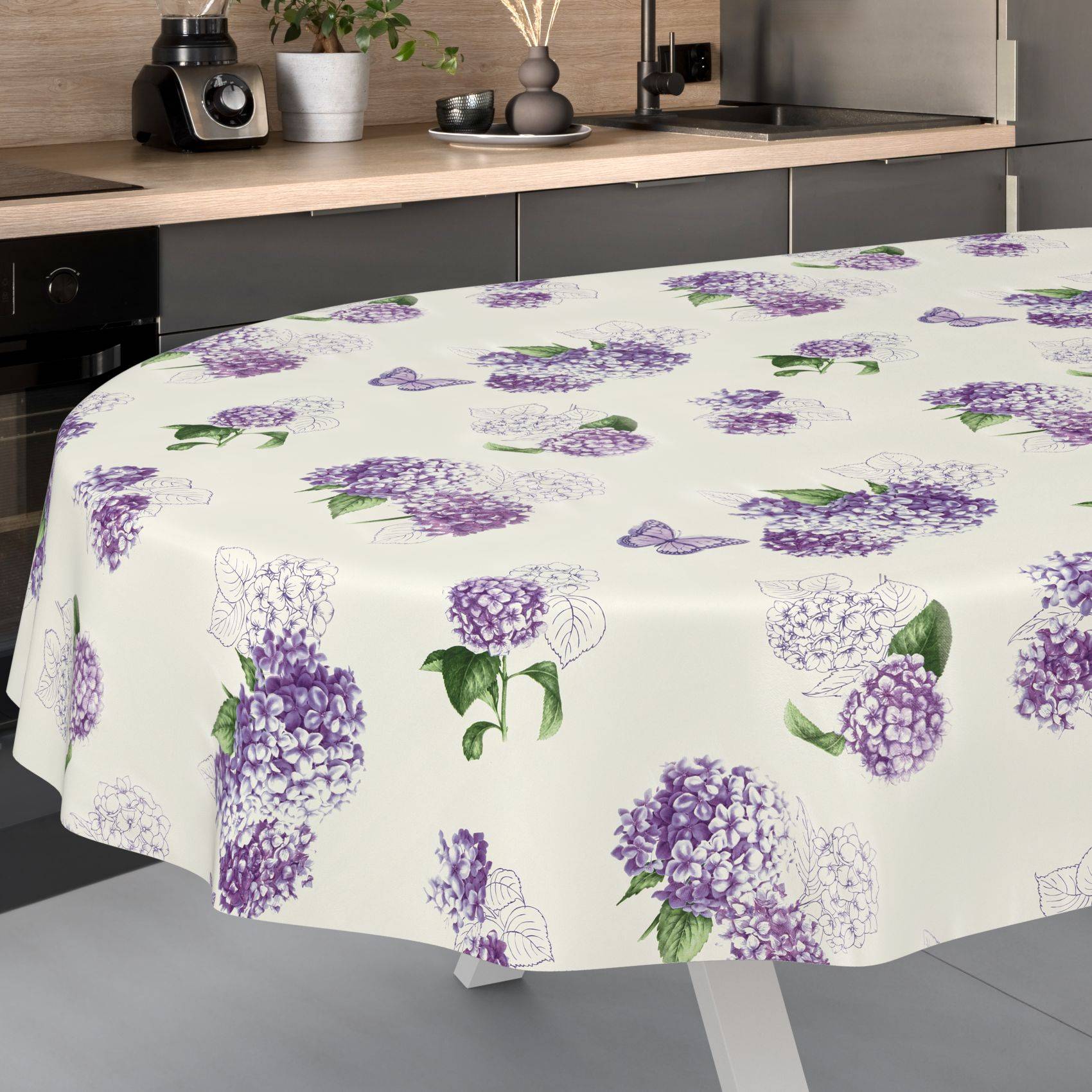 Weiße Tischdecke mit verstreuten violetten Hortensienbüten und grünen Blättern über einen Esstisch in einer modernen Küche drapiert.