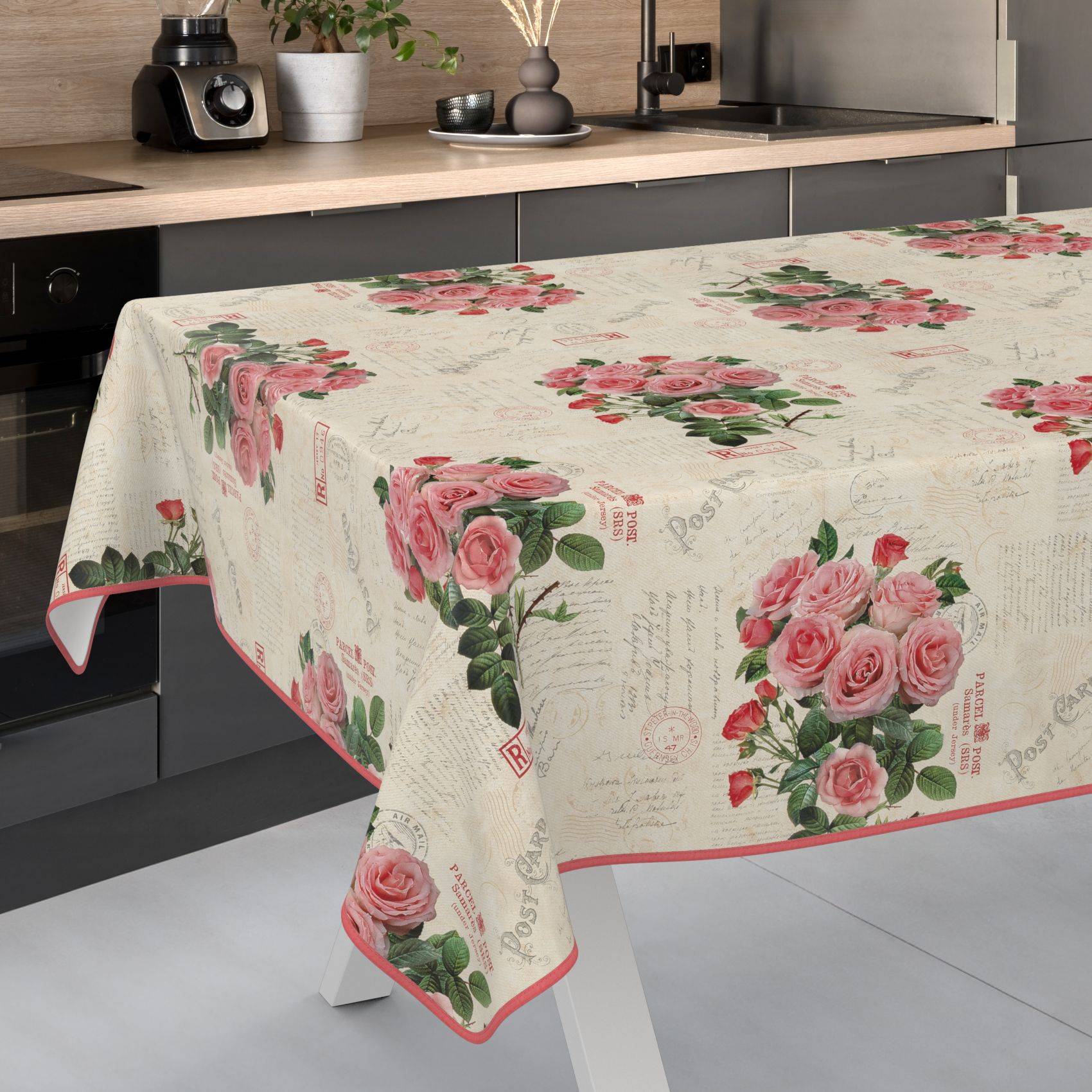 Blumige Tischdecke mit rosafarbenen Rosensträußen und Vintage-Schriftmuster, das über einen Küchentisch in einer modernen Küche drapiert ist.