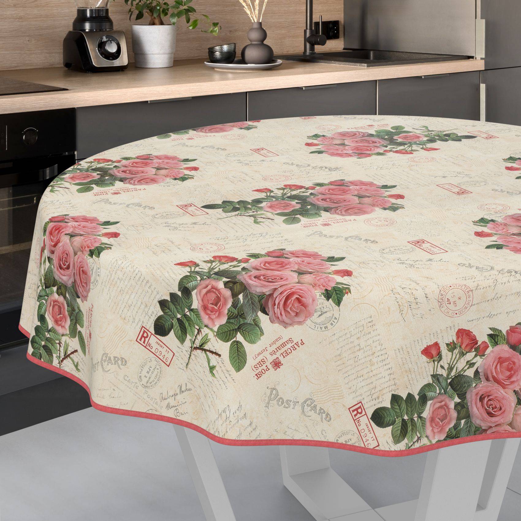 Runder Küchentisch mit einer cremefarbenen Tischdecke mit Blumenmuster, die rosafarbene Rosen und Postkartenstil-Drucke zeigt.