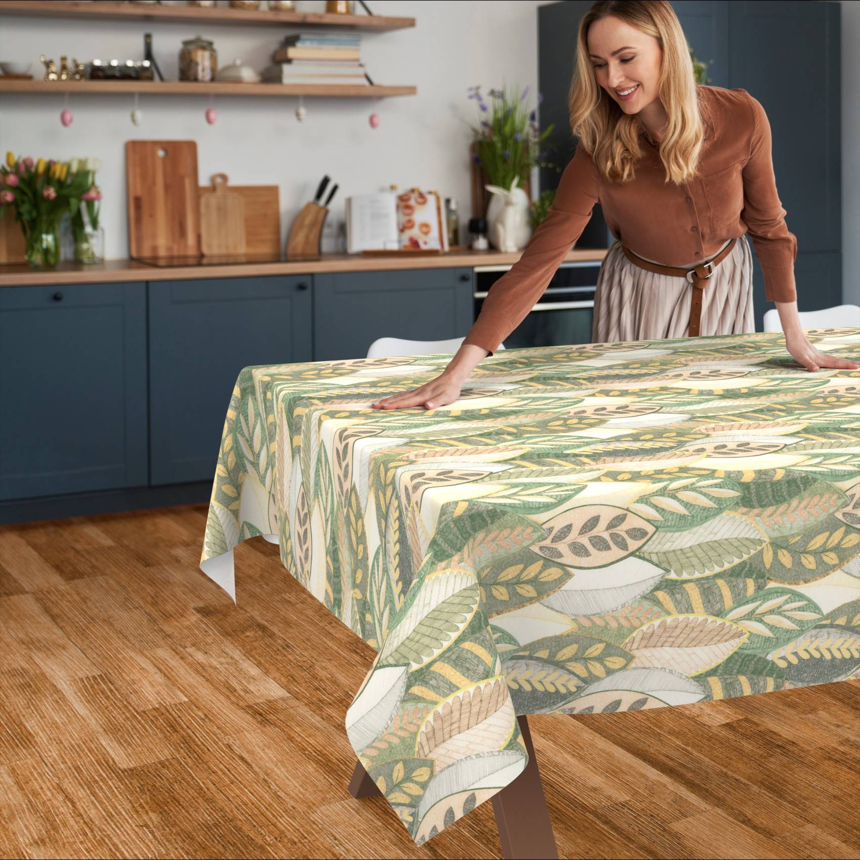 Frau, die ein Tischdecke mit Blattmuster über einen Esstisch in einer Küche glättet.