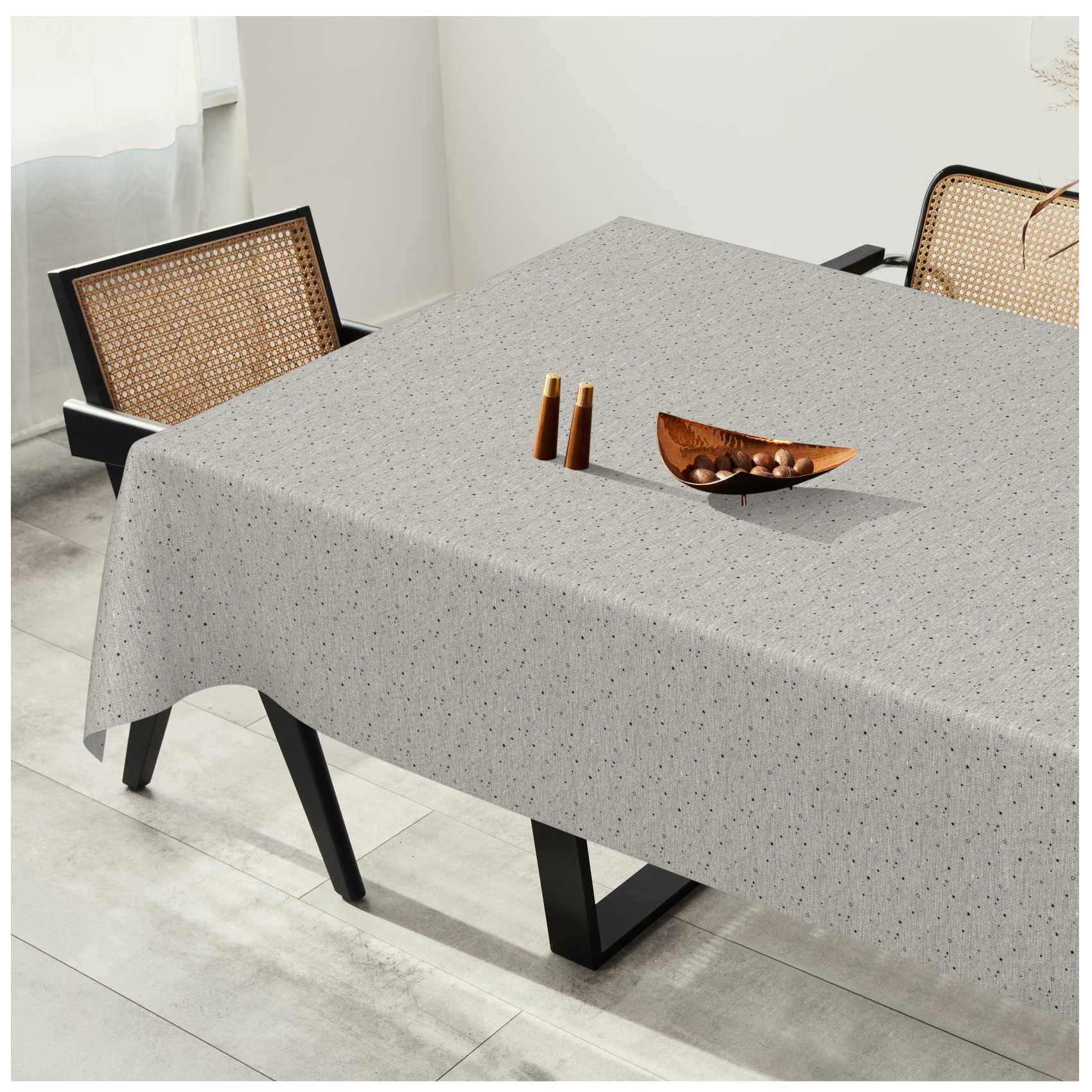 Esstisch mit einer hellgrauen gesprenkelten Tischdecke, zwei hölzernen Streubüchsen und einer dekorativen Schüssel, flankiert von Stühlen mit gewebtem Rückenlehnen in einem hellen Raum.
