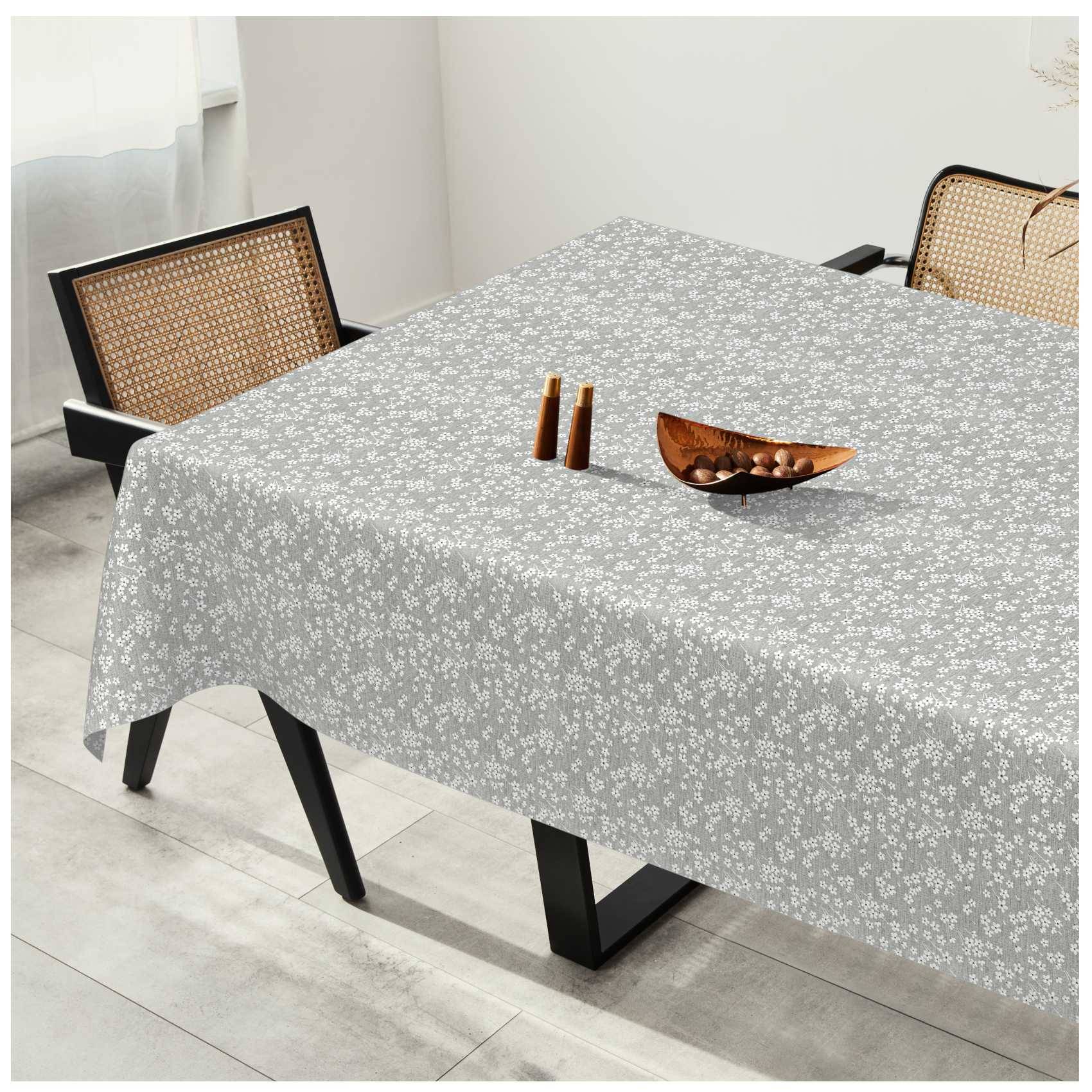 Esstisch mit grauer Blumenschutzdecke, zwei Stühle mit Rohrrücken und eine Holzschale mit kleinen Dekorationsgegenständen.