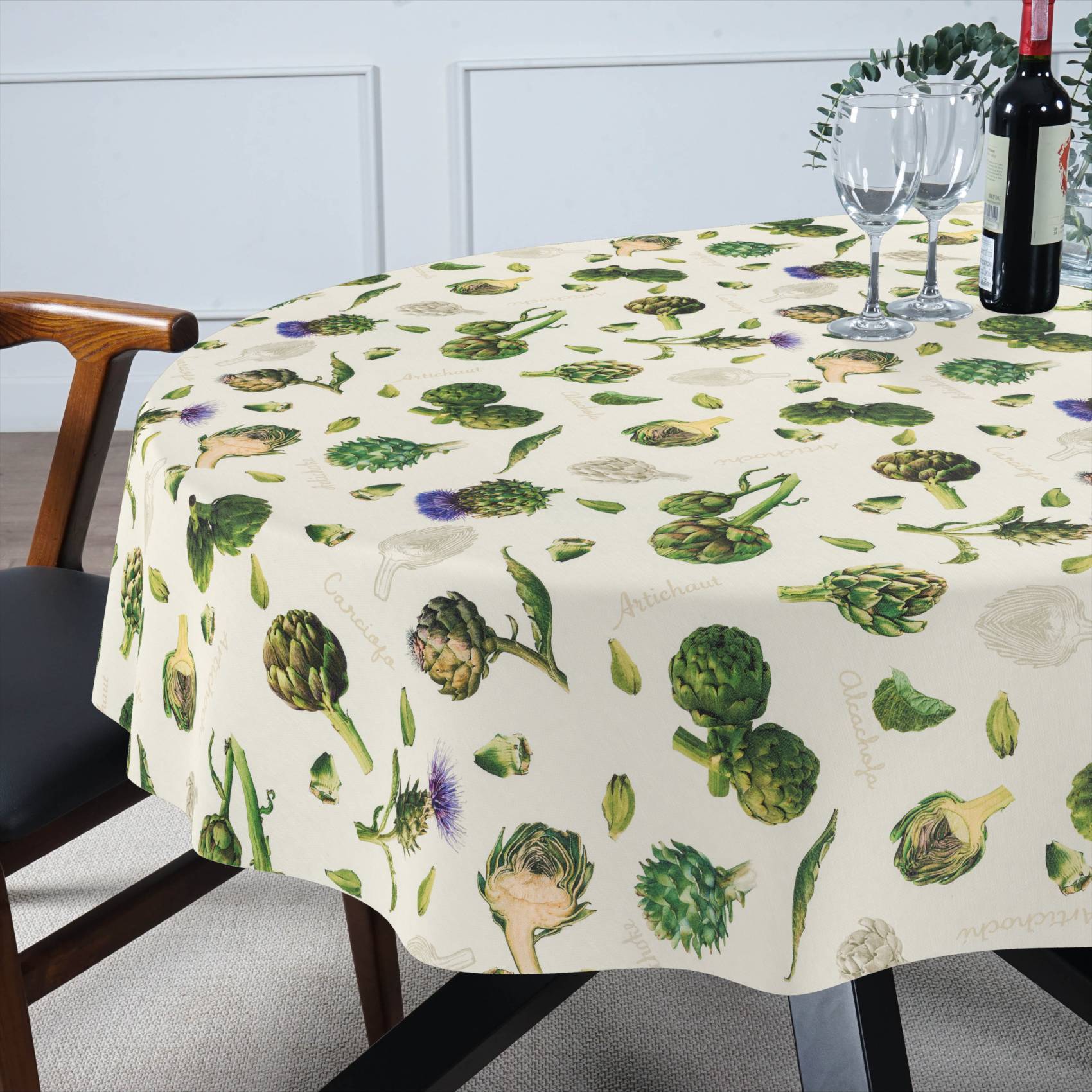 Runder Esstisch mit einer Tischdecke mit Artischockenmuster, eingedeckt mit Weingläsern und einer Flasche neben einem Stuhl.