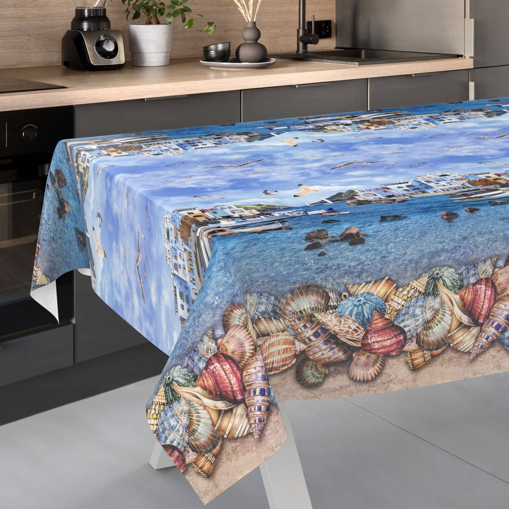 Tischdecke mit Strandszene und Muschelborte, die über einen Küchentisch drapiert ist.