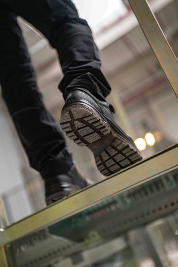 Nahaufnahme einer Person, die eine Treppe hinuntergeht, zeigt einen schwarzen Schuh, der auf einer Glasstufe tritt, mit der Sohle, die von unten sichtbar ist.