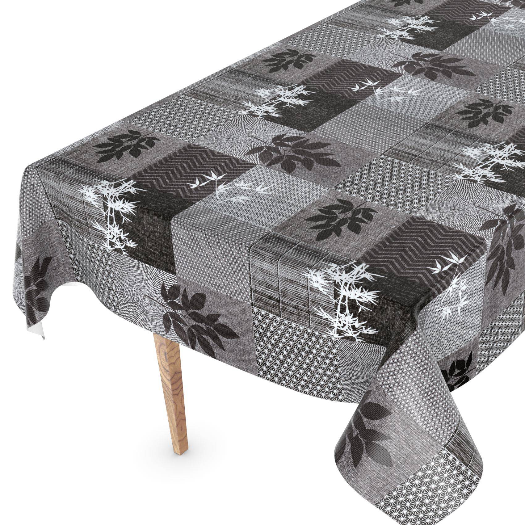 Ein grauer Patchwork-Tischdecke mit Blatt- und geometrischen Mustern liegt über einem Tisch und ist vor weißem Hintergrund dargestellt.