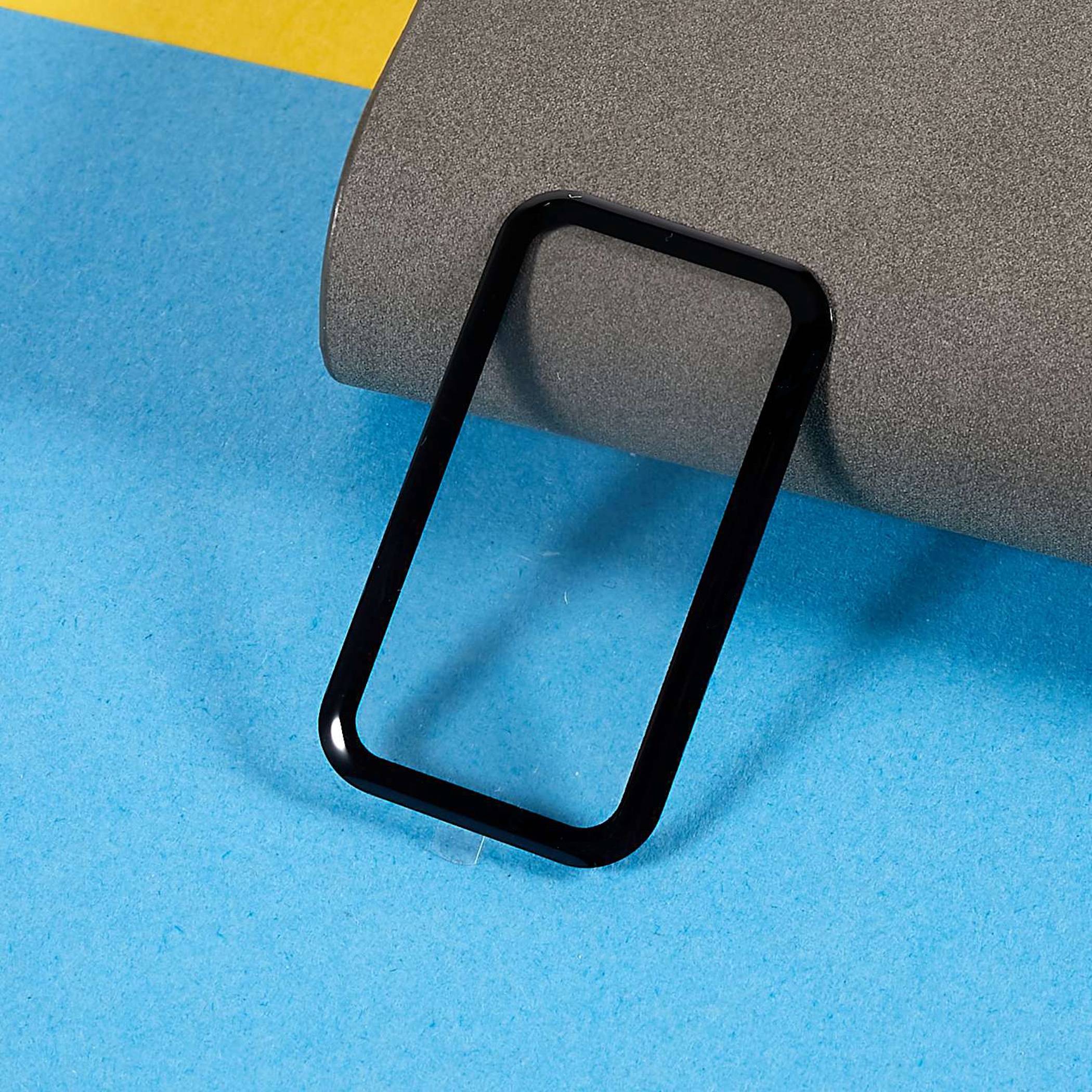 Schwarze Smartphone-Hülle oder Rahmen, der an einer grauen gerollten Matte auf blauem und gelbem Hintergrund lehnt.