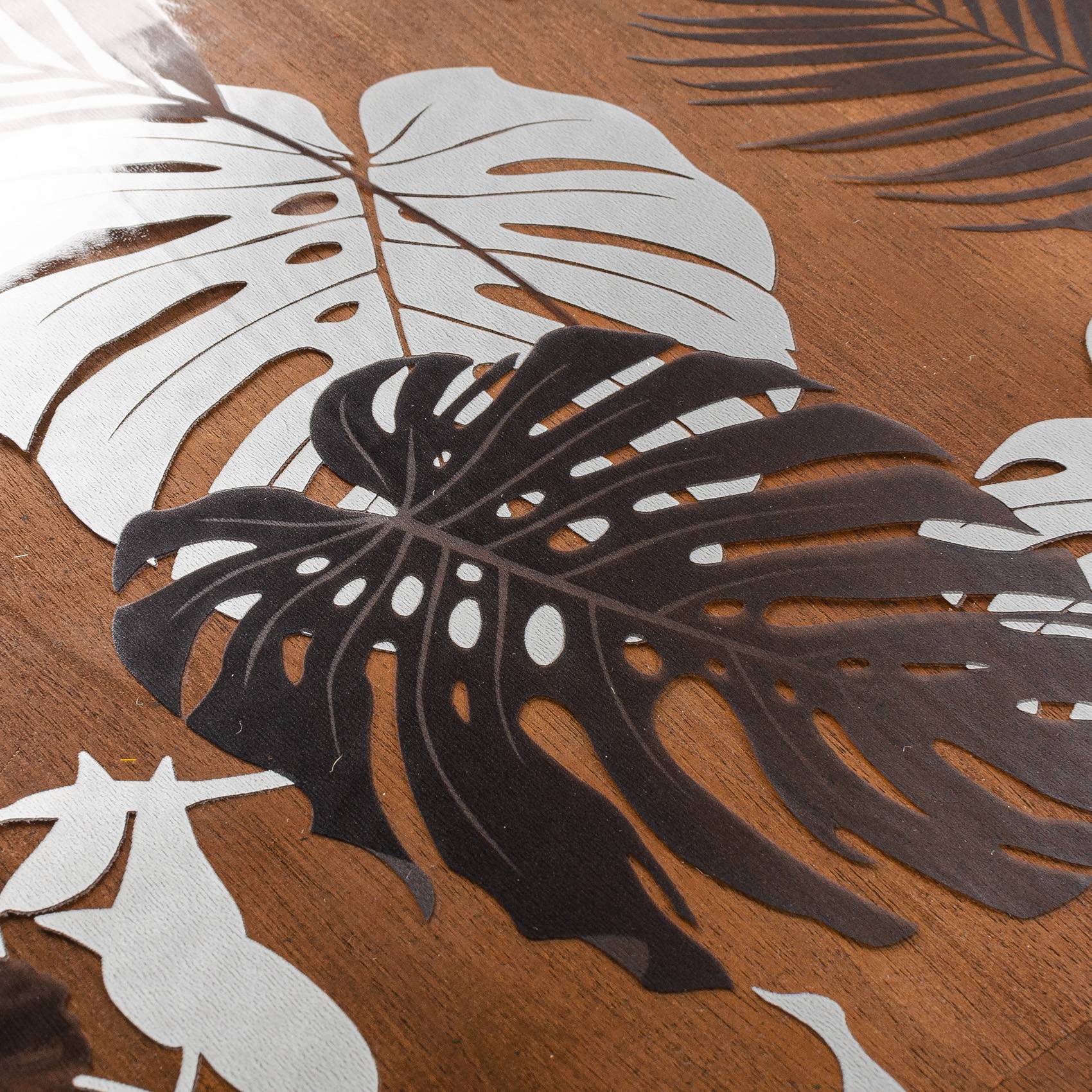 Schwarzweiße Monstera-Blattausschnitte, schichtig auf einer Holzoberfläche angeordnet, mit Sonnenlicht, das Palmenwedel-Schatten wirft.