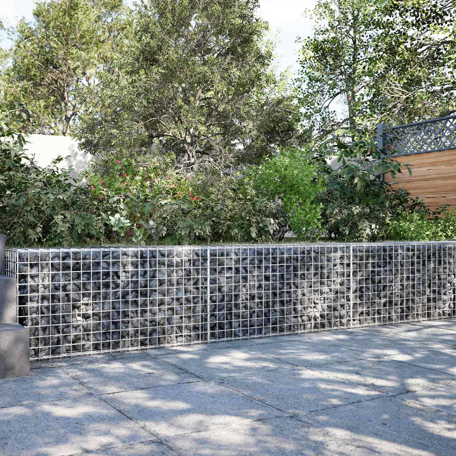Drahtgefüllte Stützmauer aus Steinen entlang eines Gehwegs mit dichten Bäumen und Sträuchern dahinter in einer privaten Außenanlage einer Wohnanlage.