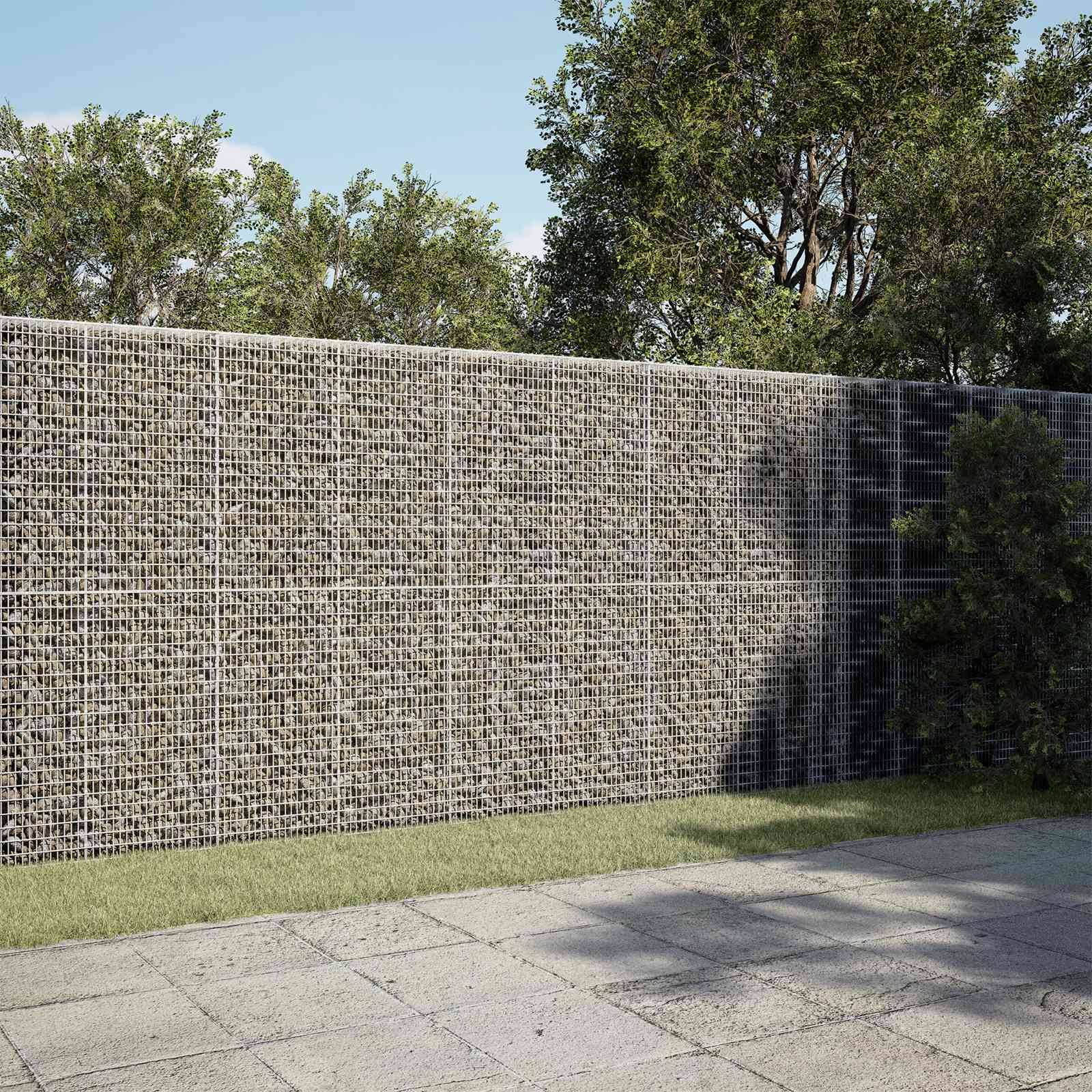 Große Schanzkorb-Steinmauer, die einen gestalteten Hof abschirmt, mit Bäumen dahinter und einer gepflasterten Terrasse im Vordergrund.