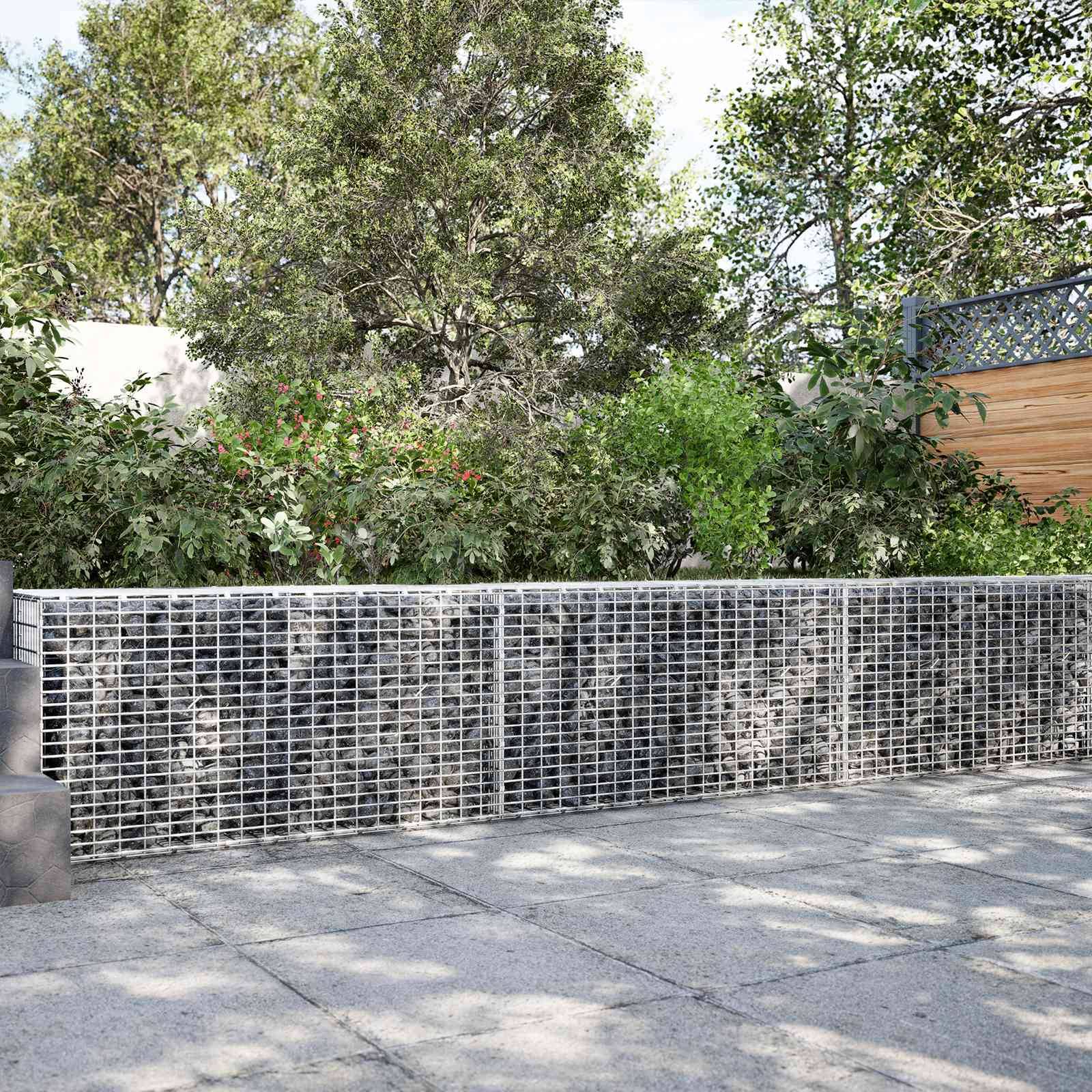 Outdoor-Gartenweg mit einer niedrigen Drahtgitter-Stützmauer vor dichten Bäumen und Sträuchern, die gefleckte Schatten auf das Pflaster werfen.