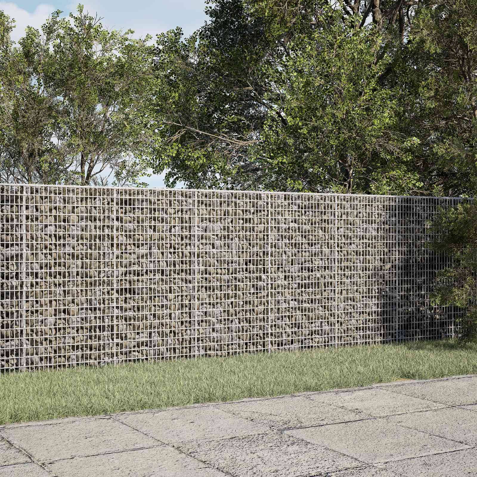 Gabionen-Steinmauer entlang eines grasbewachsenen Gehwegs, mit Bäumen und Laub dahinter.