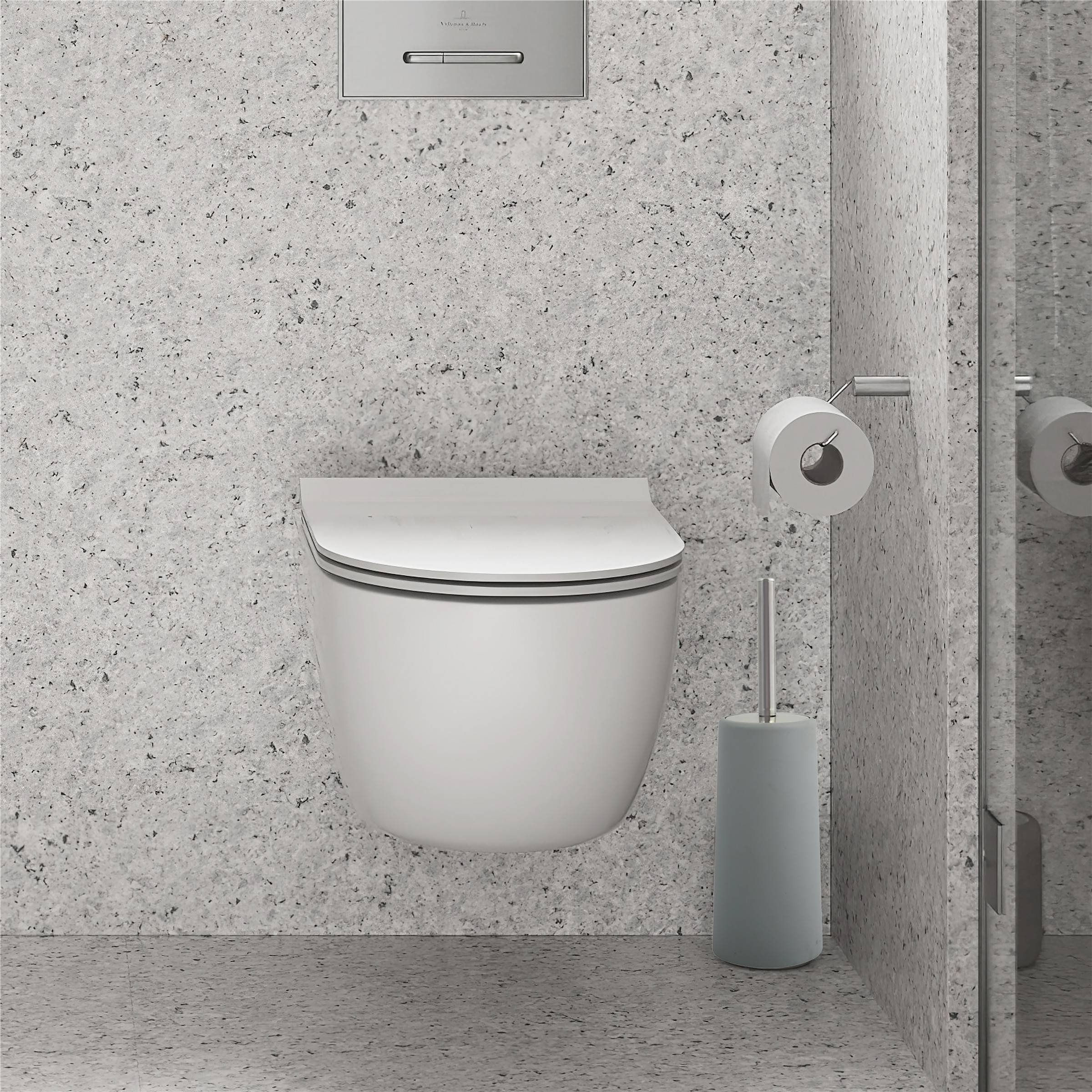 Modernes an der Wand montiertes Toilettenbecken in einem minimalistischen Badezimmer, mit einem Toilettenbürsten-Behälter daneben und einer Spülplatte darüber.