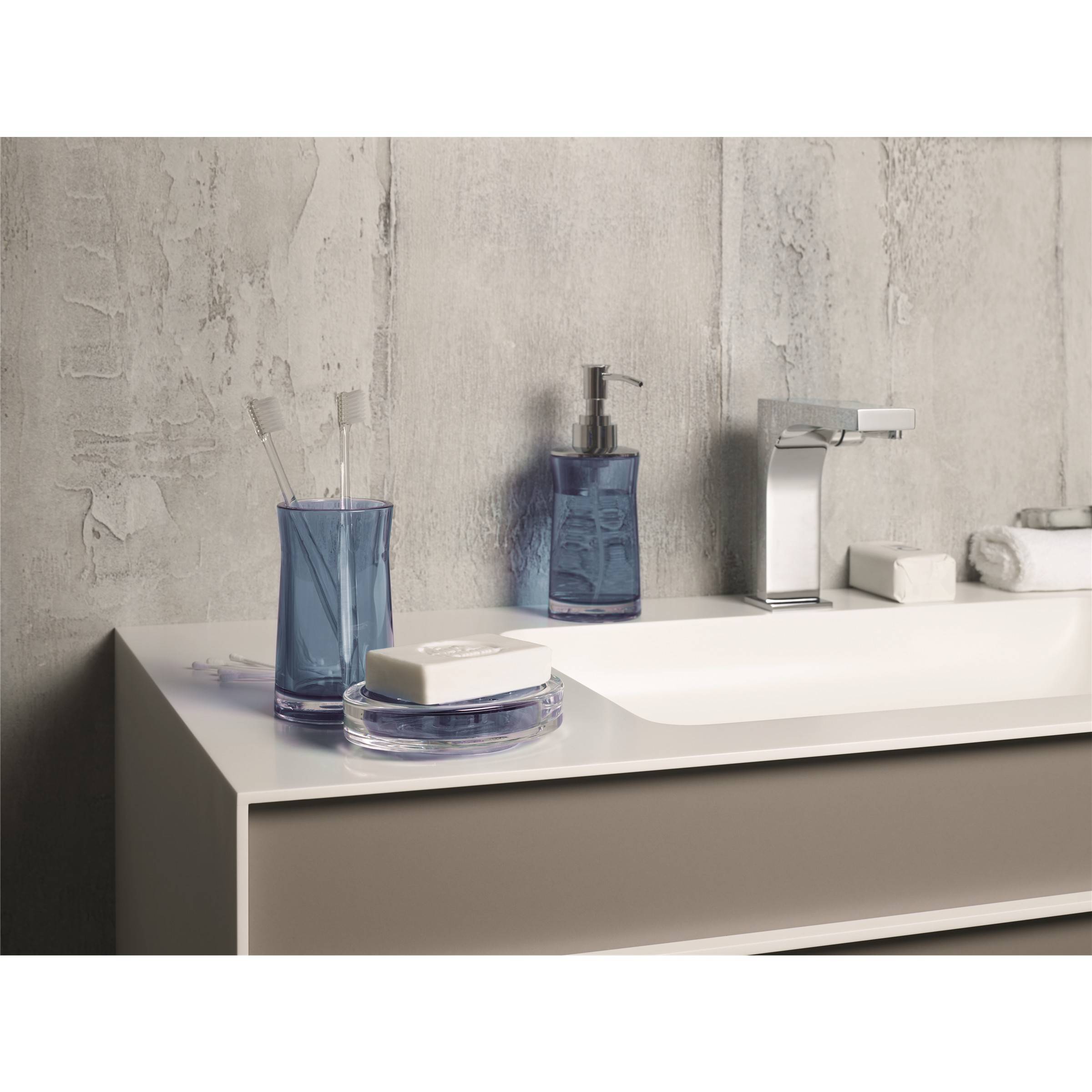 Modernes Badezimmerwaschtisch mit Waschbecken und Chromarmatur, blaue Seifenspender und Zahnbürstenhalter sowie gefaltete Handtücher vor einer strukturierten grauen Wand.