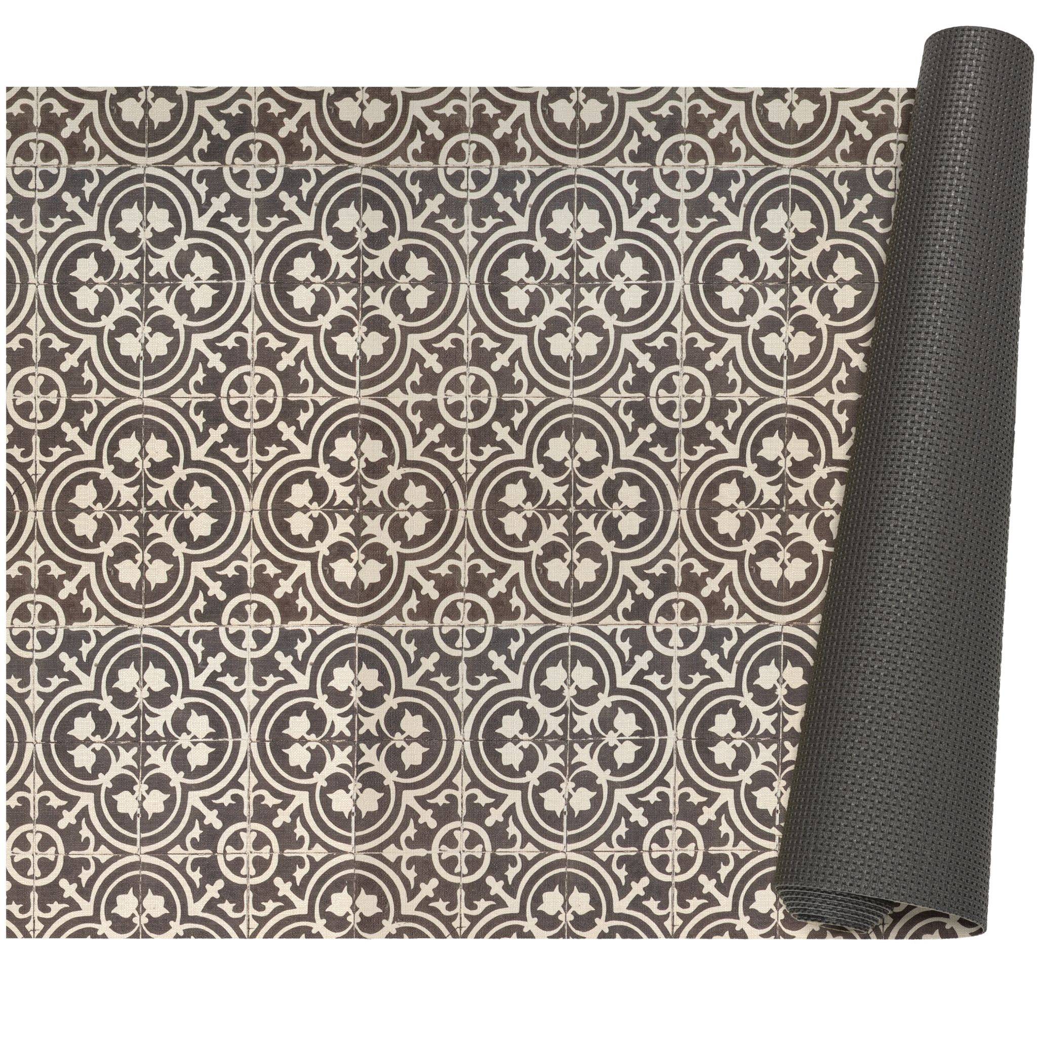 Gerollte schwarze strukturierte Matte neben einer flachen braun-cremefarbenen Fläche mit ornamentalem geometrischem Fliesenmuster.