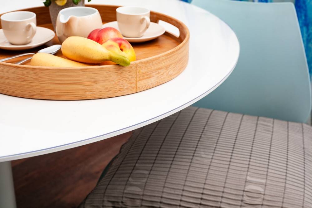 Teabrett mit vier Tassen und Obst auf einem runden Tisch neben einem karierten Stuhl