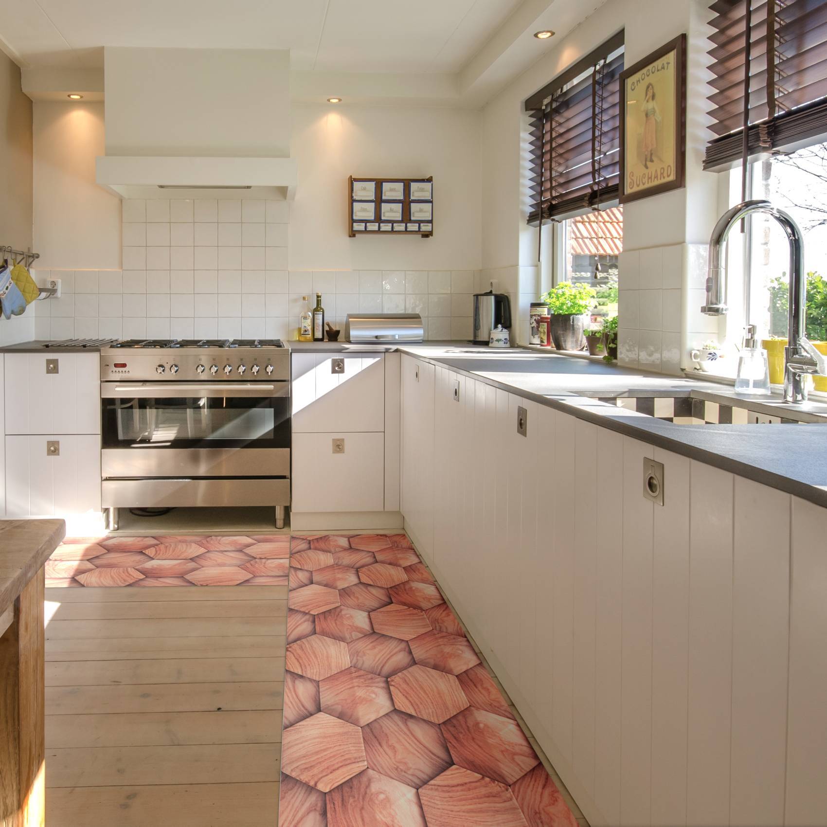 Helle moderne Küche mit Edelstahlofen, weißen Schränken, langer Arbeitsplatte, Spüle bei Fenstern mit Jalousien und gemustertem Teppich auf Holzboden.