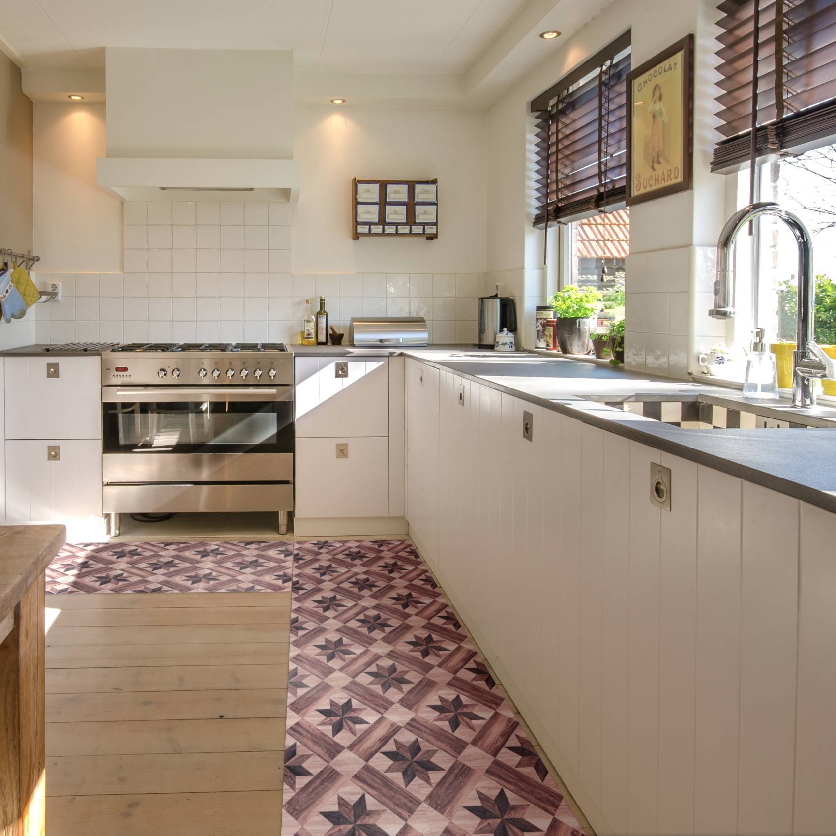 Helle moderne Küche mit weißen Schränken, Edelstahlofen, langer Arbeitsplatte, Spüle am Fenster und gemustertem Läufer auf dem Boden.