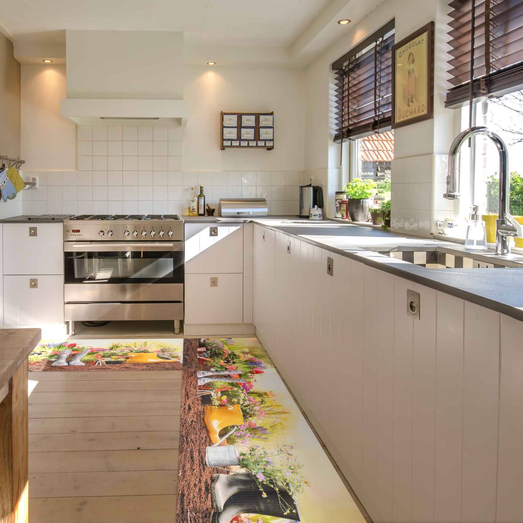 Helle moderne Küche mit Edelstahlofen, weißen Schränken, langer Arbeitsplatte und Spüle am Fenster, mit bunten Blumenteppichen auf dem Boden.